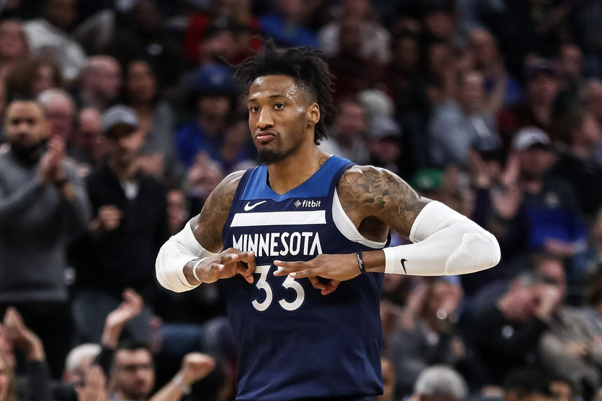 robert covington 桌布 壁紙 — 一位身穿藍色球衣、背號33的明尼蘇達灰狼籃球球員在比賽中自信地做手勢，背景是模糊的人群。