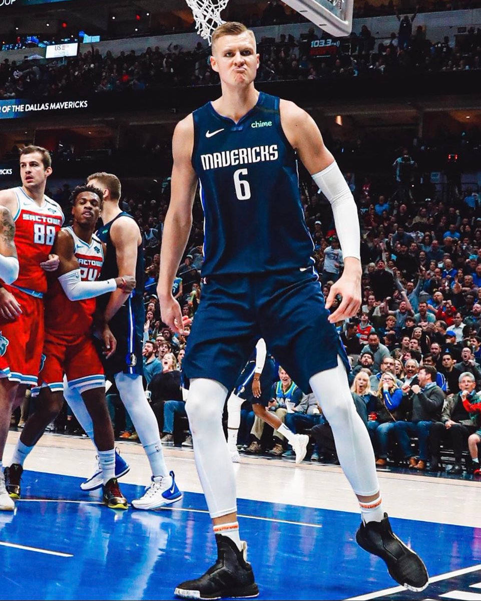 Kristaps Porzingis 桌布 壁紙 — 一位身穿藍色球衣6號的達拉斯獨行俠籃球運動員，在座無虛席的比賽中自信地站在充滿活力的藍色球場上。