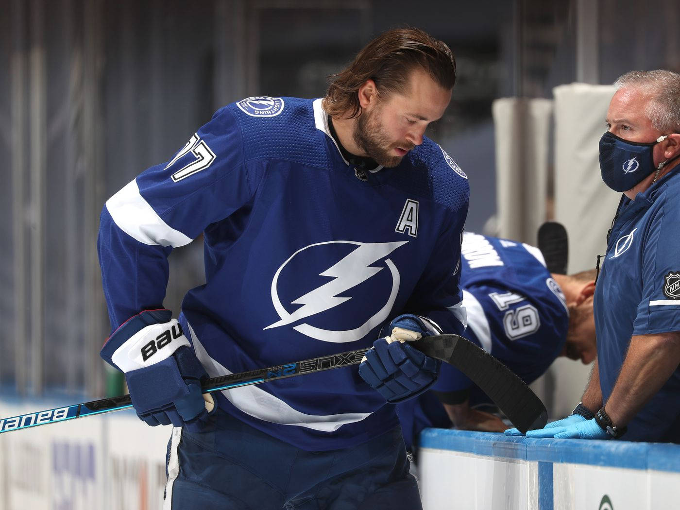 hockey 桌布 壁紙 — 一位身穿藍色球衣的坦帕灣閃電冰球球員靠在冰場圍板上，手持球棍，旁邊有一位戴著口罩的教練在觀看。