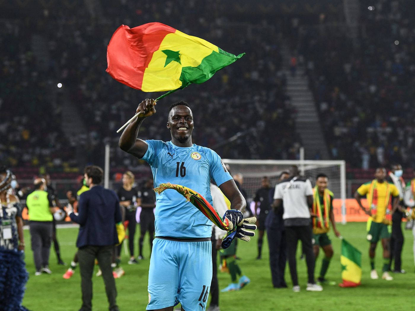 Senegal 桌布 壁紙 — 一位身穿藍色球衣的塞內加爾足球守門員在燈光璀璨的球場上勝利地揮舞著國旗。