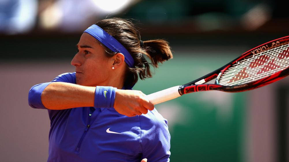 Tennis 桌布 壁紙 — 一位身穿藍色球衣的女網球選手在明亮的陽光下，在紅土球場上專注地揮拍。