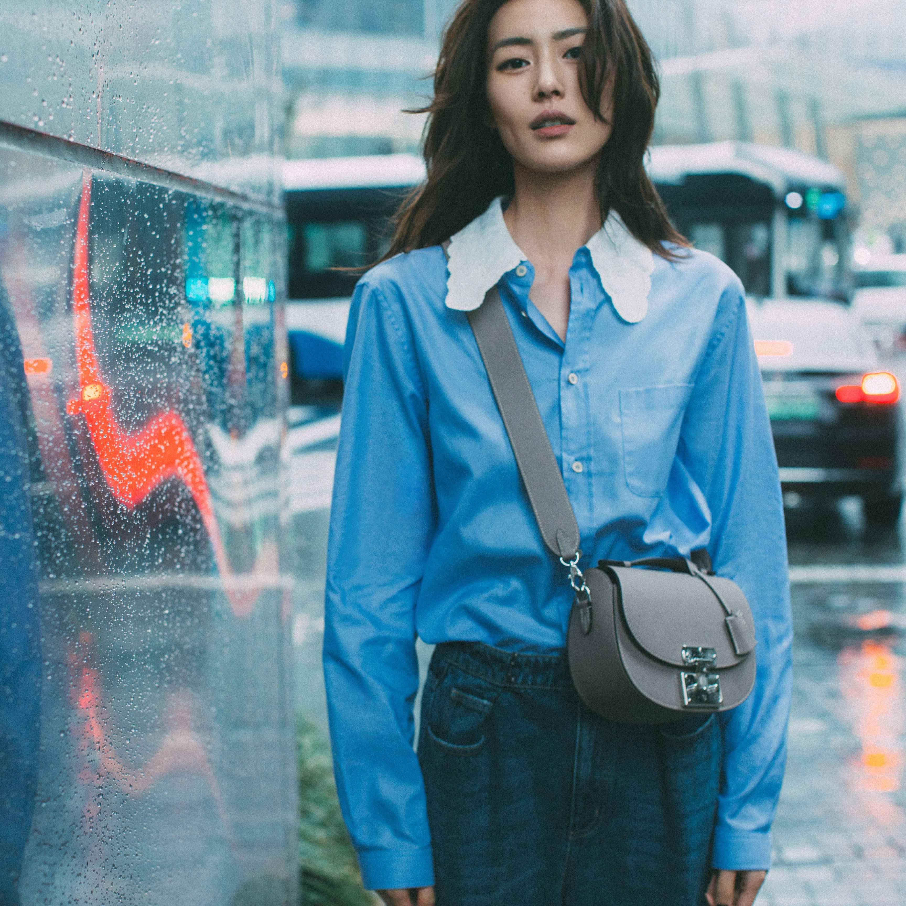 美女 桌布 壁紙 — 一位身穿藍色白領襯衫的女性，在夜晚的城市街道上站在濺滿雨水的窗邊。