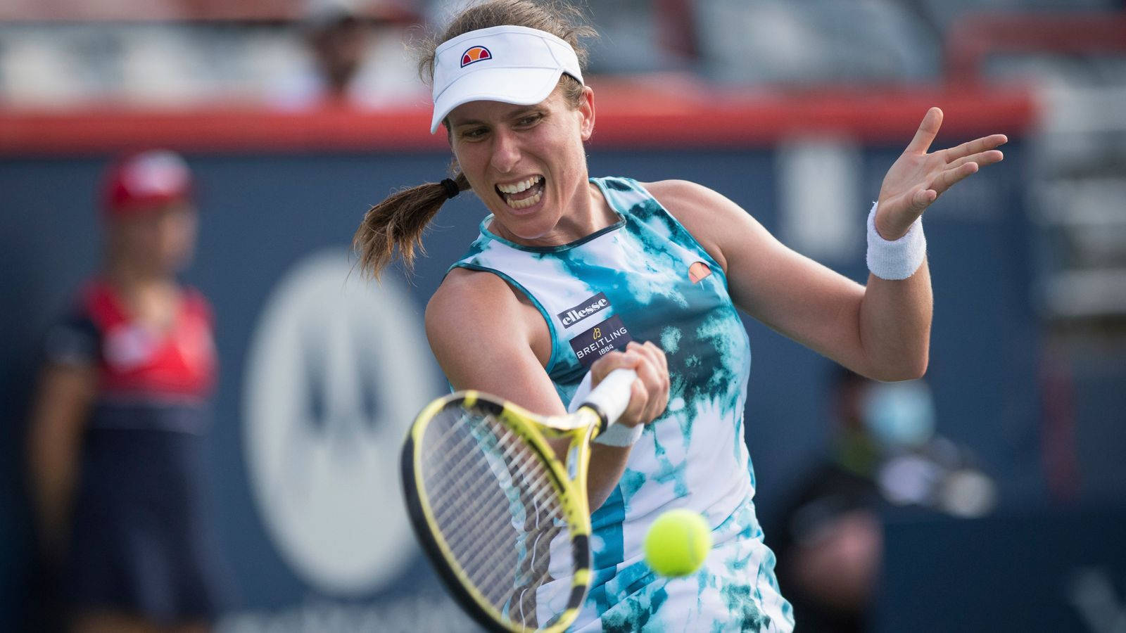 Athletic 桌布 壁紙 — 一位身穿藍色紮染服裝的女網球選手在比賽中專注地揮拍擊打一個亮黃色的網球。