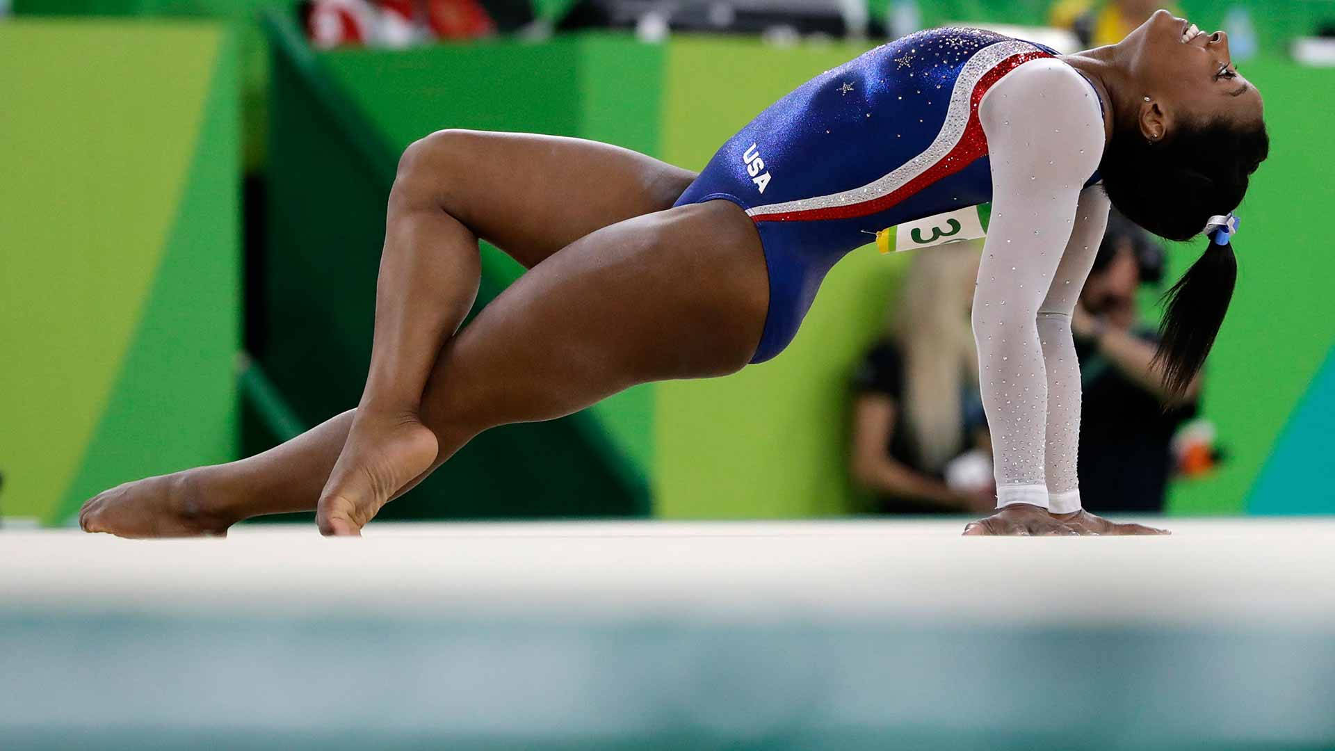 運動 桌布 壁紙 — 一位身穿藍色美國體操服的女體操運動員，以高度專注和運動能力表演動態地板動作。