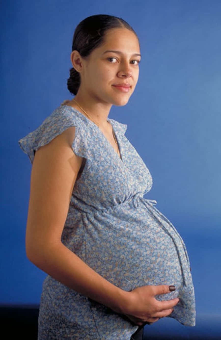 Pregnant 桌布 壁紙 — 一位身穿藍色花卉連衣裙的孕婦在純藍色攝影棚背景前輕輕地抱著她的肚子。