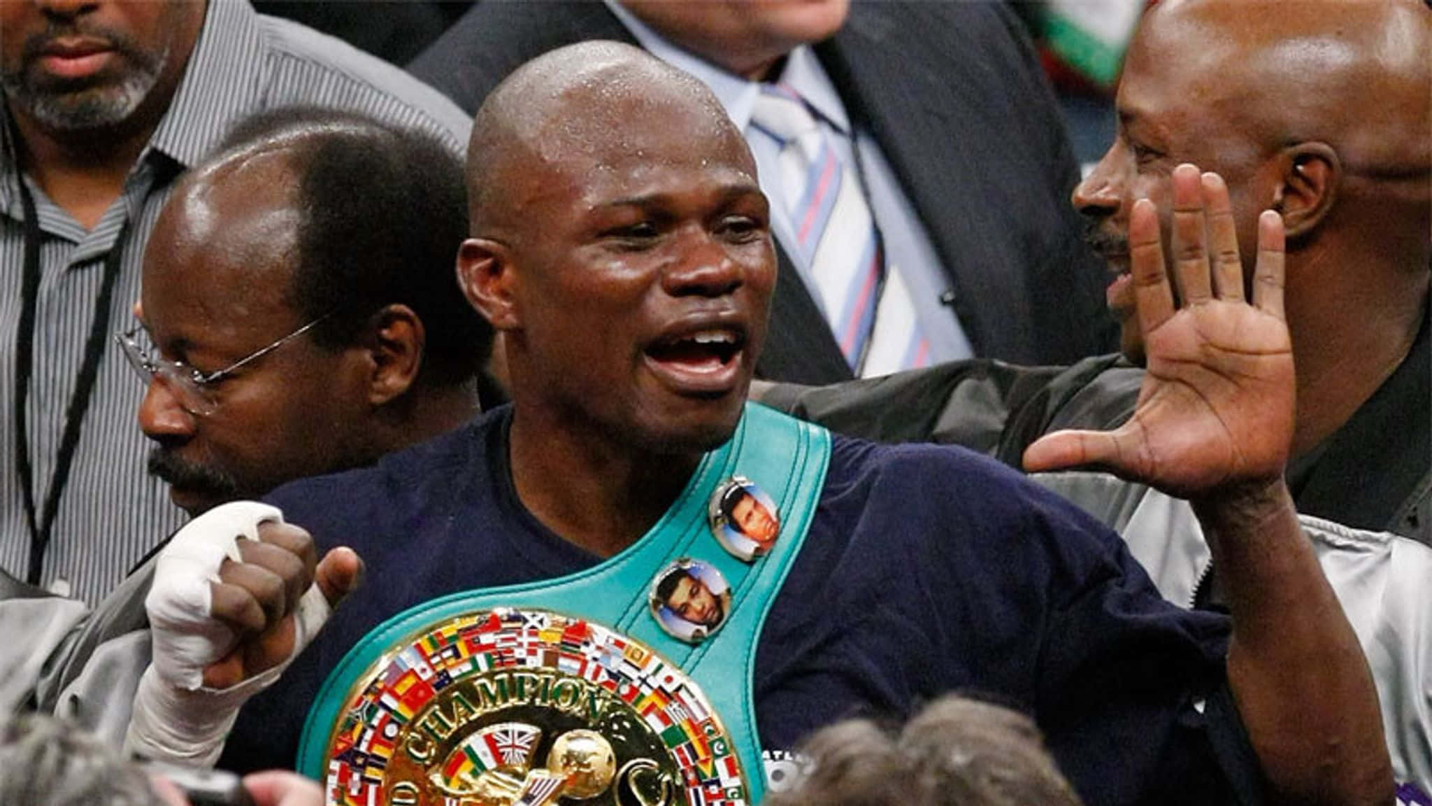 Boxing 桌布 壁紙 — 一位身穿藍色襯衫和冠軍腰帶的勝利拳擊手，在擠滿觀眾的競技場中舉起拳頭、張開嘴巴慶祝。
