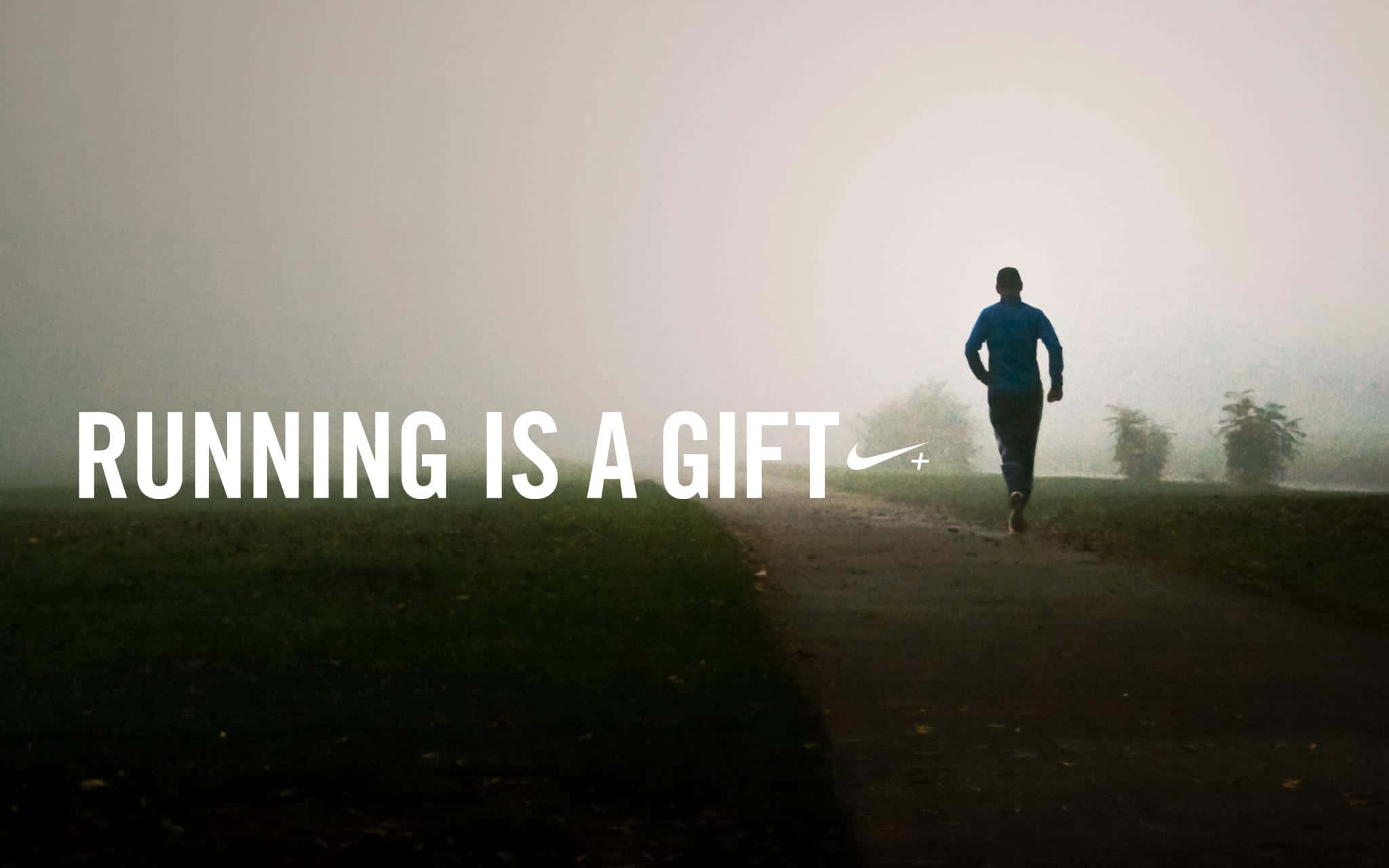 Motivation 桌布 壁紙 — 一位身穿藍色襯衫的孤獨跑者，在霧氣瀰漫的小徑上向著發光的地平線前進，文字為running is a gift。