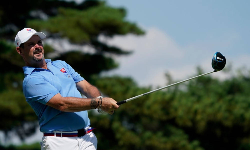 Golfing 桌布 壁紙 — 一位身穿藍色襯衫的高爾夫球手，在綠樹和晴朗天空的背景下，專注地揮動一號木桿。