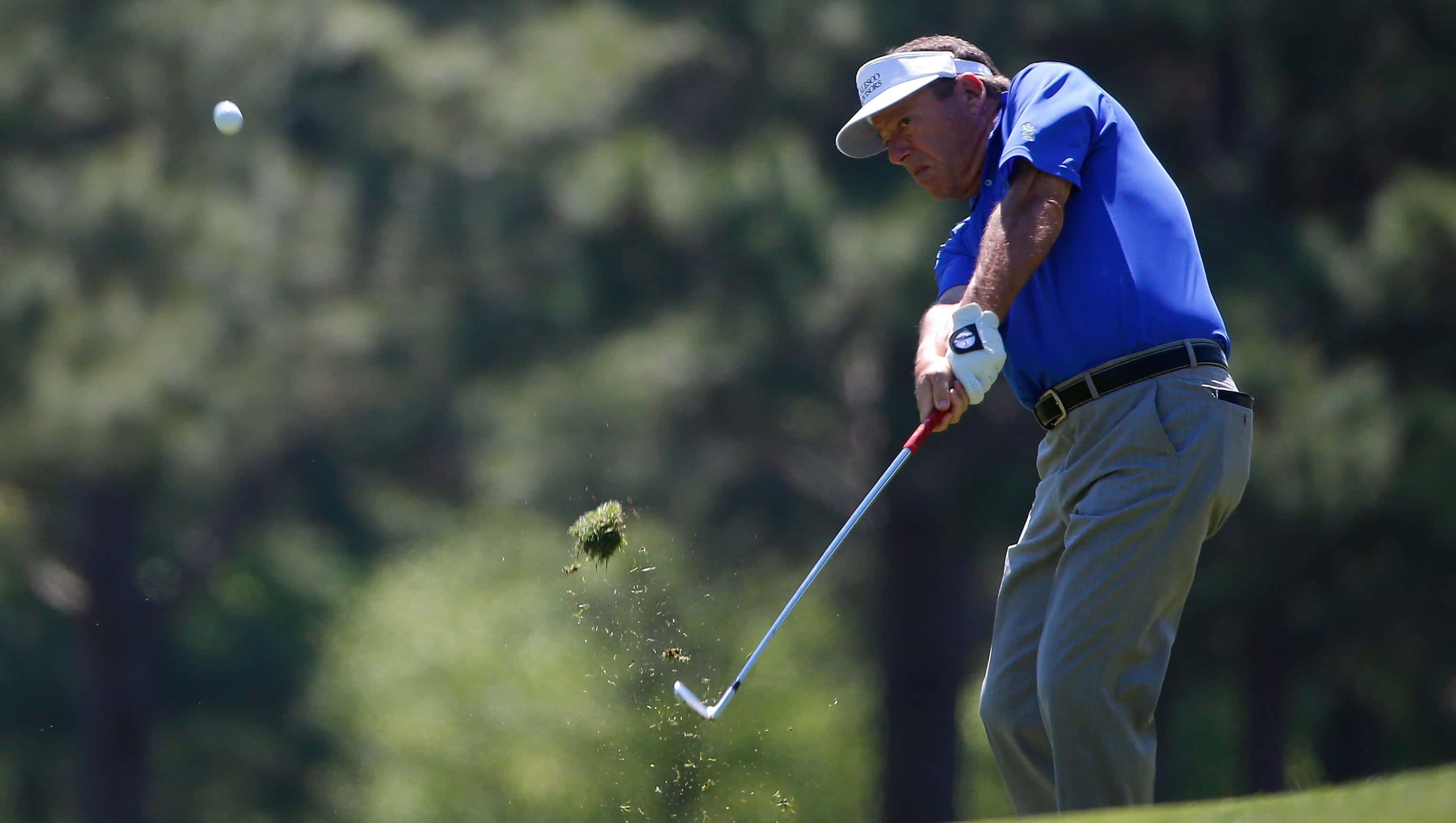 Golf Ball 桌布 壁紙 — 一位身穿藍色襯衫的高爾夫球手揮動球桿，從沙坑中擊球，草屑向上飛濺。