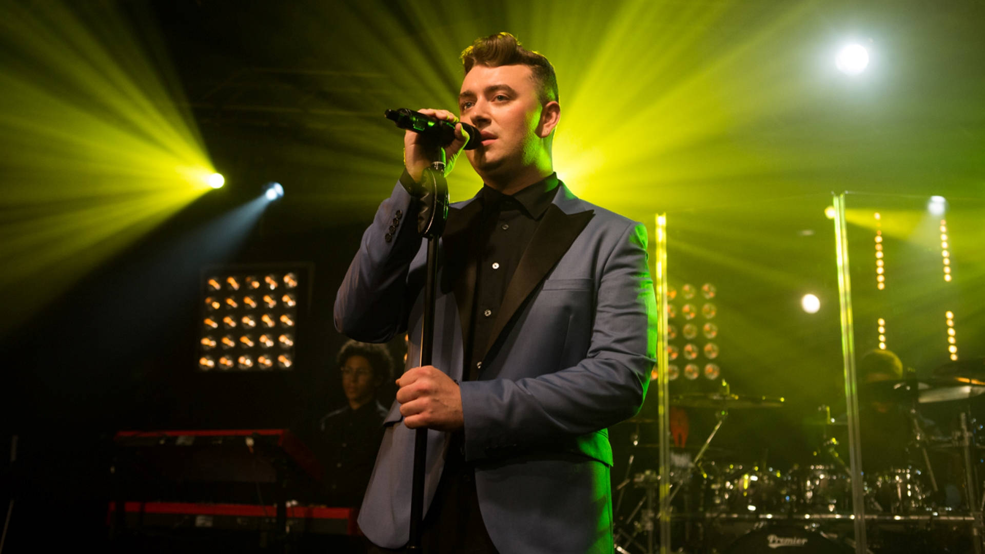 Sam Smith 桌布 壁紙 — 一位身穿藍色西裝的男歌手在充滿活力的綠色舞台燈光下，熱情地對著麥克風演唱。