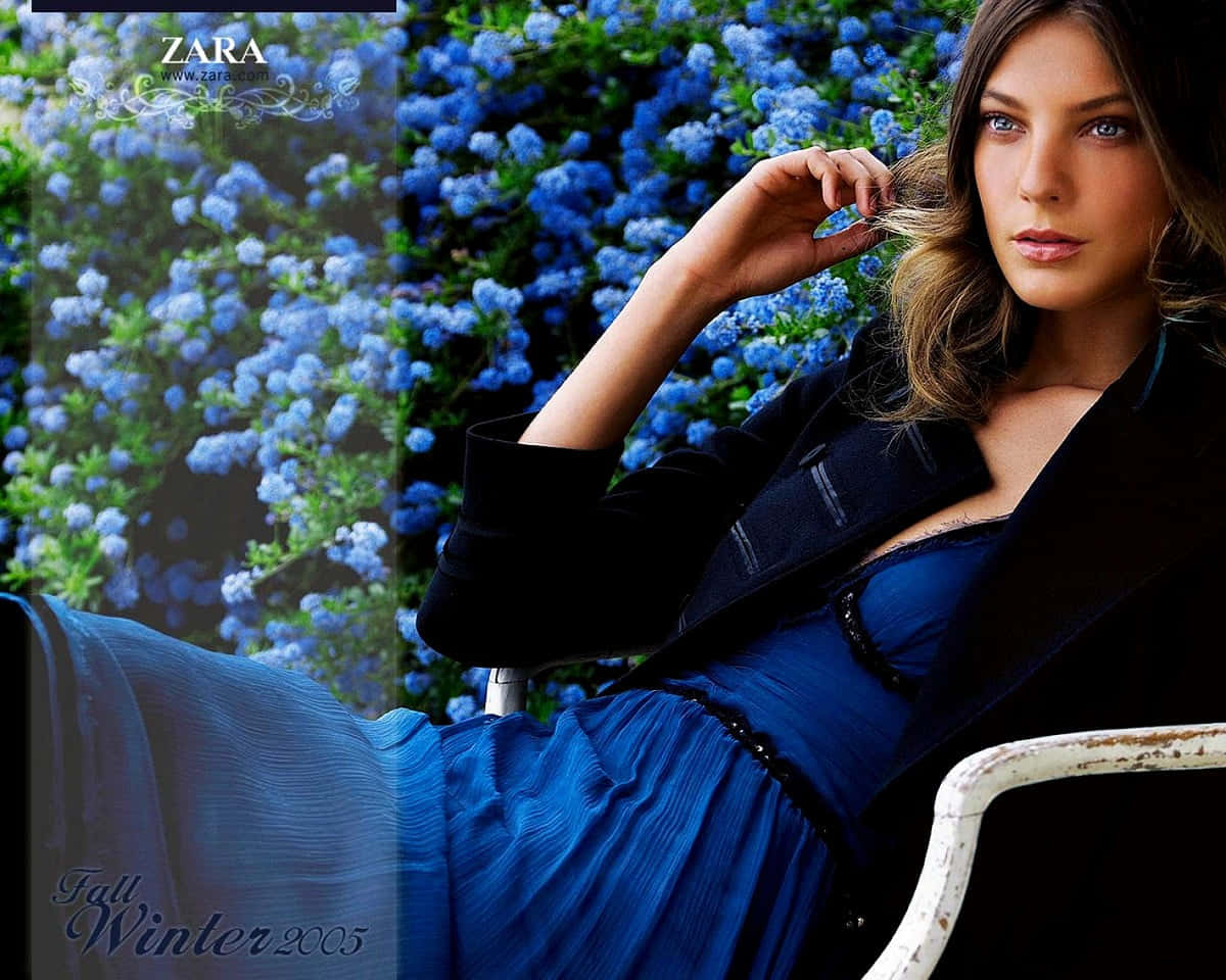 Zara 桌布 壁紙 — 一位身穿藍色連衣裙和黑色西裝外套的女性，在鮮豔藍色花朵的背景前優雅地坐著。