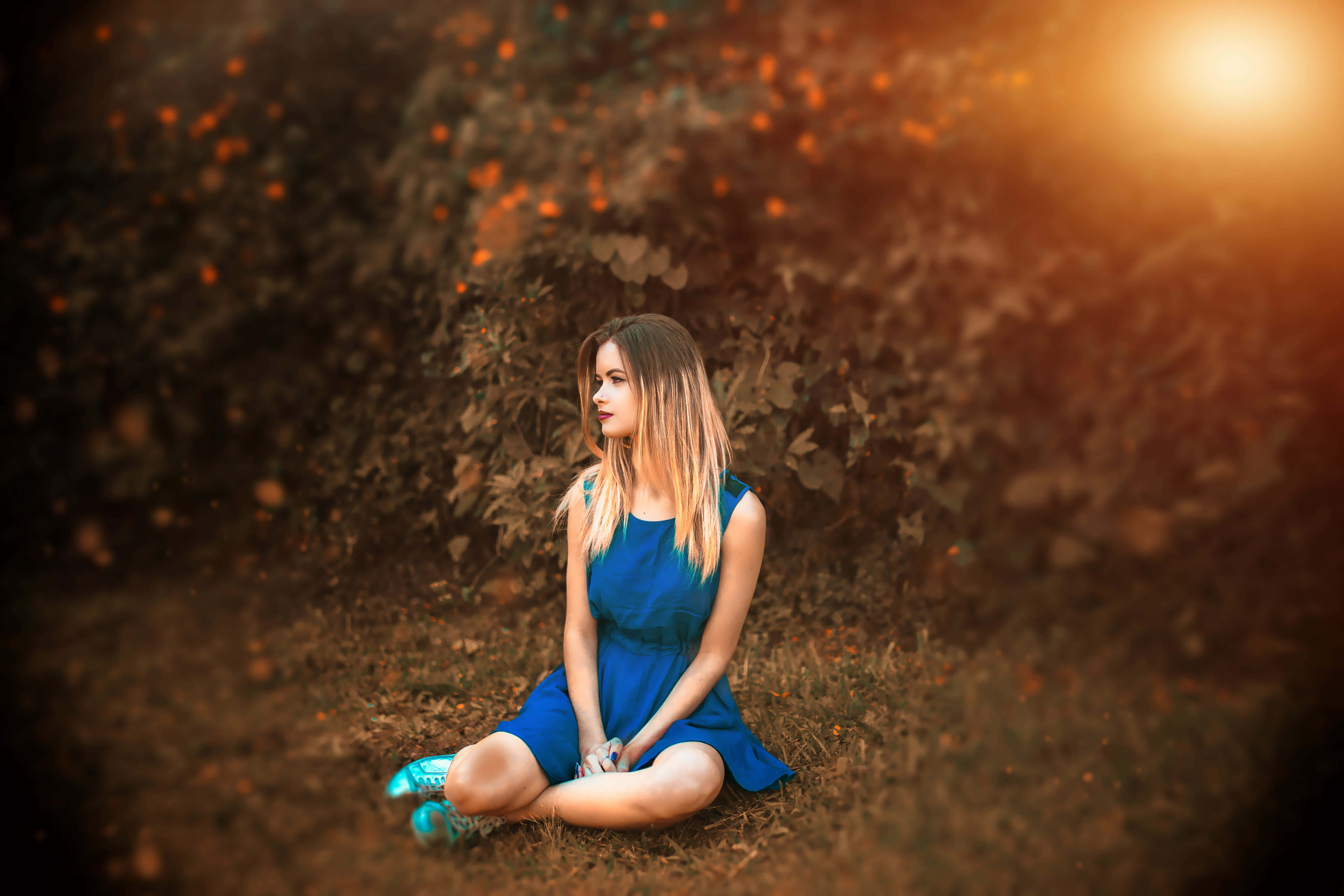 Outdoor Activities 桌布 壁紙 — 一位身穿藍色連衣裙的年輕女性盤腿坐在秋天的落葉上，金色的陽光穿過周圍的樹葉灑落下來。