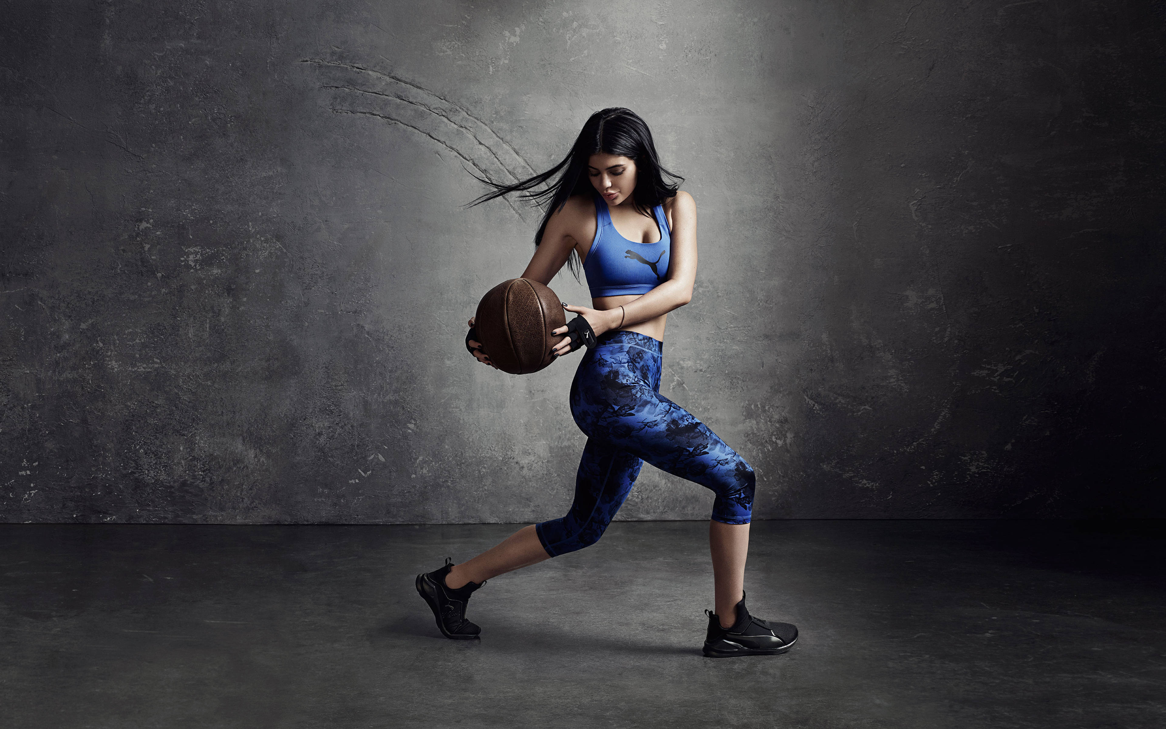 Kylie 桌布 壁紙 — 一位身穿藍色運動服的女性，在帶有紋理的灰色工作室牆前，以動態動作運球。