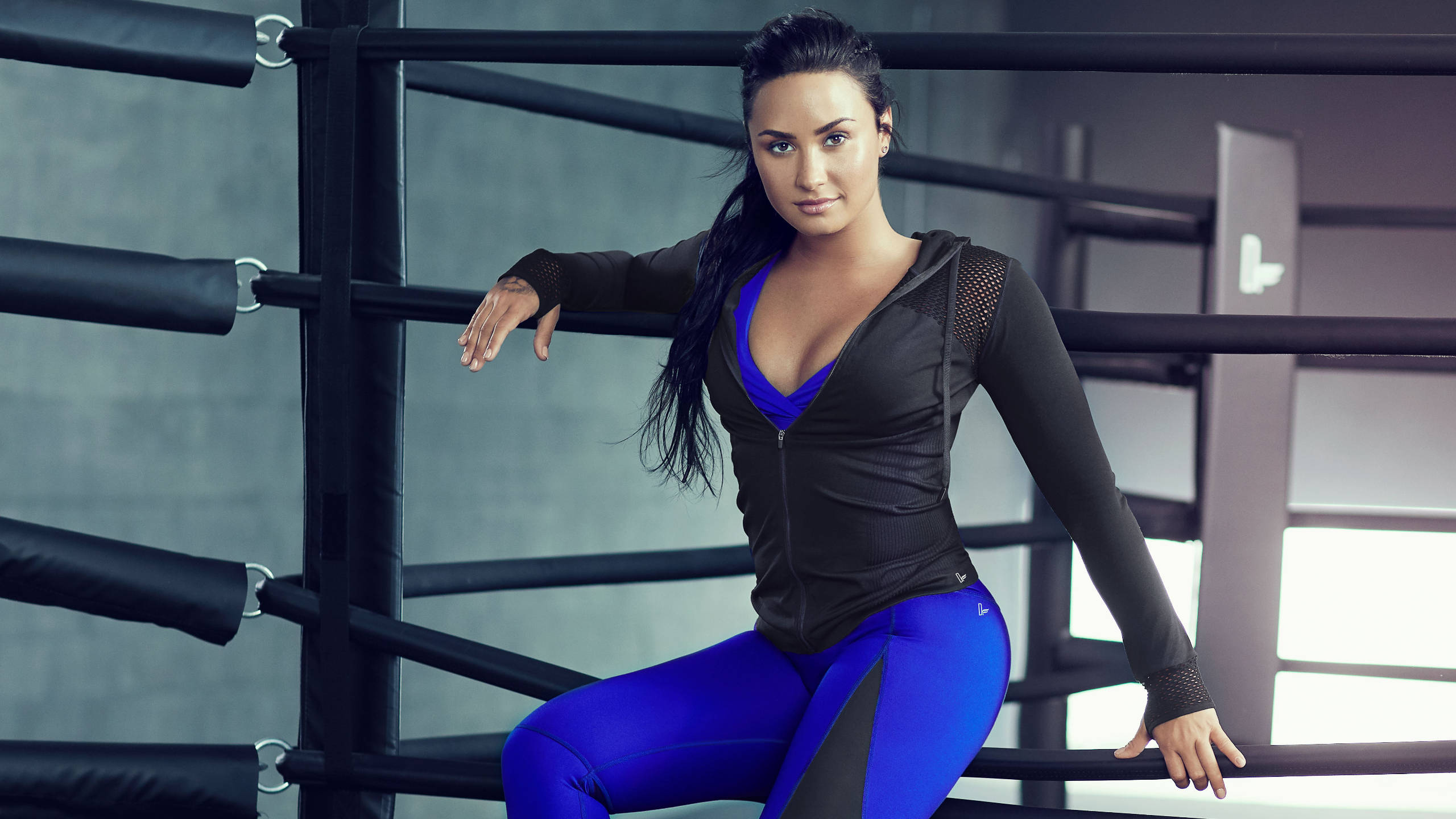 demi 桌布 壁紙 — 一位身穿藍色運動服的女性在黑色繩索和灰色牆壁的拳擊場內自信地擺姿勢。