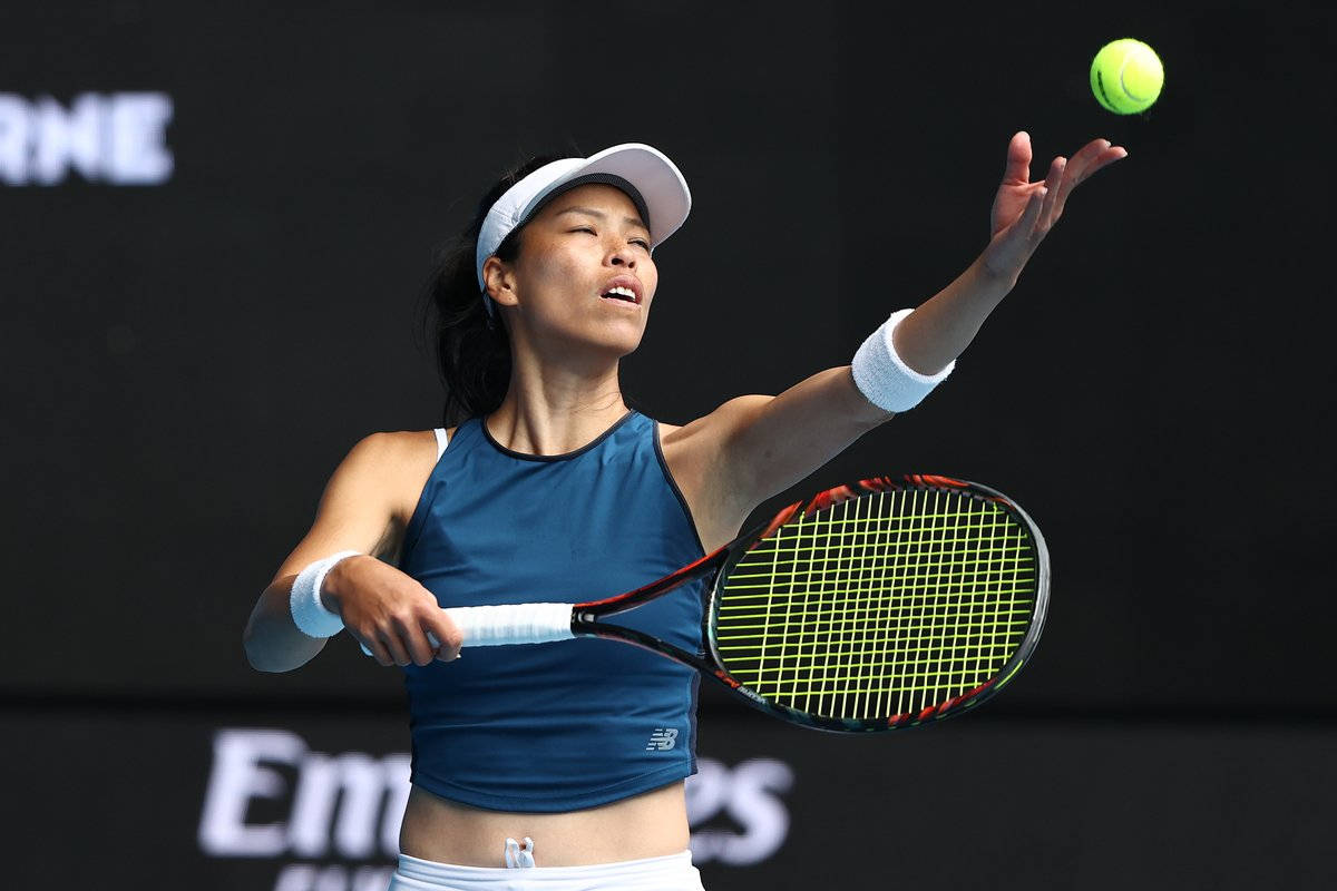 網球 桌布 壁紙 — 一位身穿藍色運動服的女性網球選手將一顆亮黃色的球拋向空中，準備以高度專注的狀態發球。