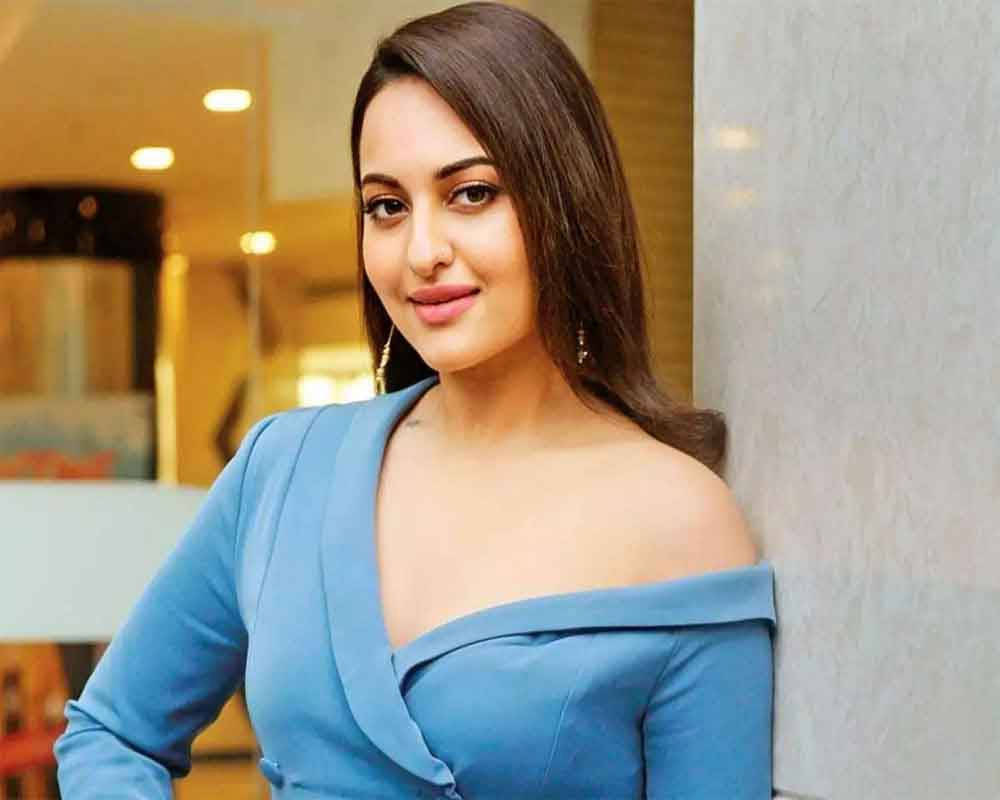 Sonakshi Sinha 桌布 壁紙 — 一位身穿藍色露肩連衣裙的女性靠在牆上，身後有溫暖的室內燈光。