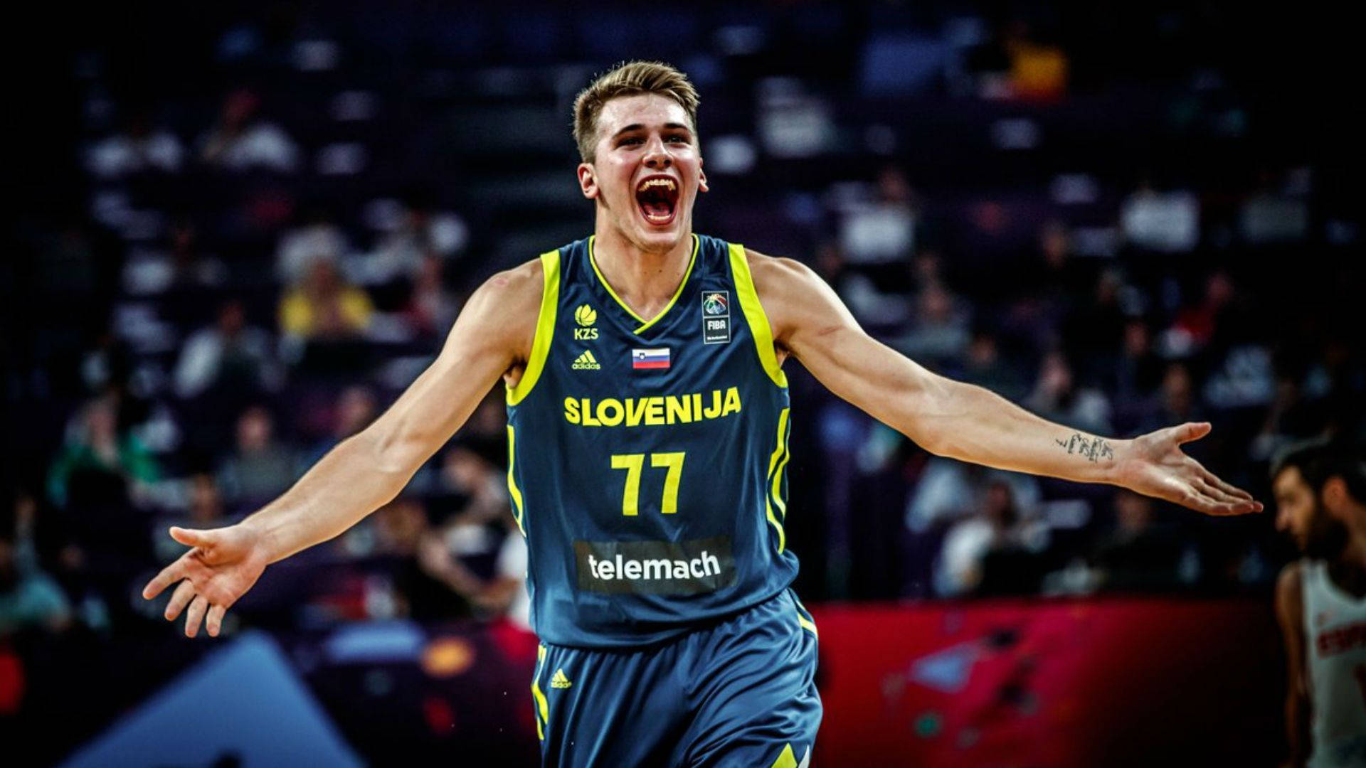 Luka 桌布 壁紙 — 一位身穿藍黃球衣、背號77的斯洛維尼亞籃球運動員在球場上張開雙臂慶祝勝利。