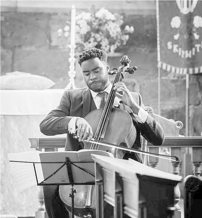 cello 桌布 壁紙 — 一位身穿西裝、專注的大提琴手在石牆教堂內全神貫注地演奏他的樂器。