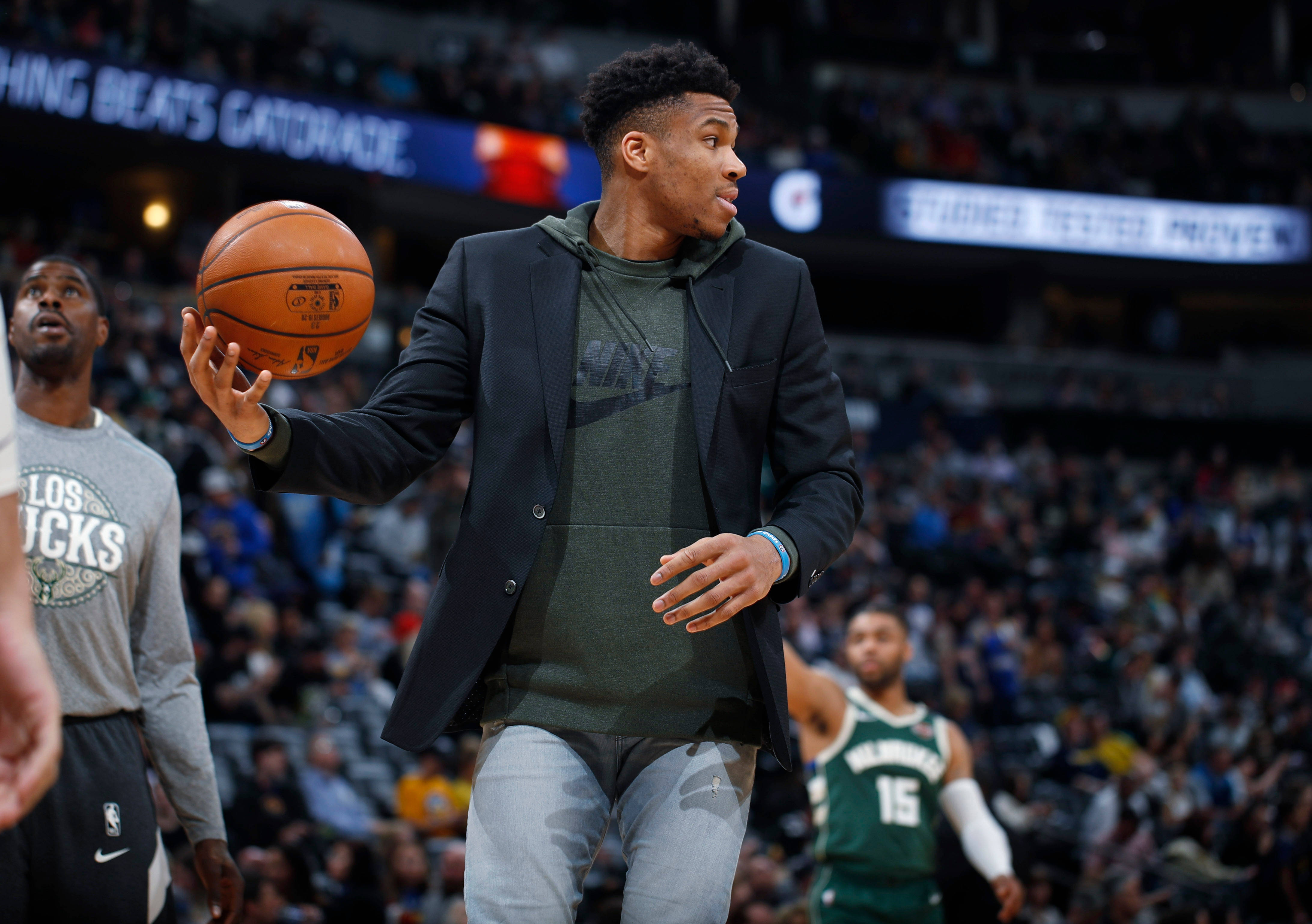 Giannis 桌布 壁紙 — 一位身穿西裝外套的籃球運動員在比賽中運球，身後是座無虛席的體育館。