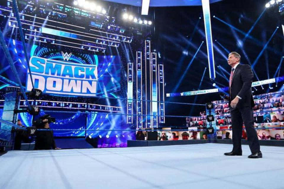 Wrestling Ring 桌布 壁紙 — 一位身穿西裝的WWE SmackDown主持人站在摔角擂台邊緣，背後有明亮的藍色舞台燈光和大螢幕。
