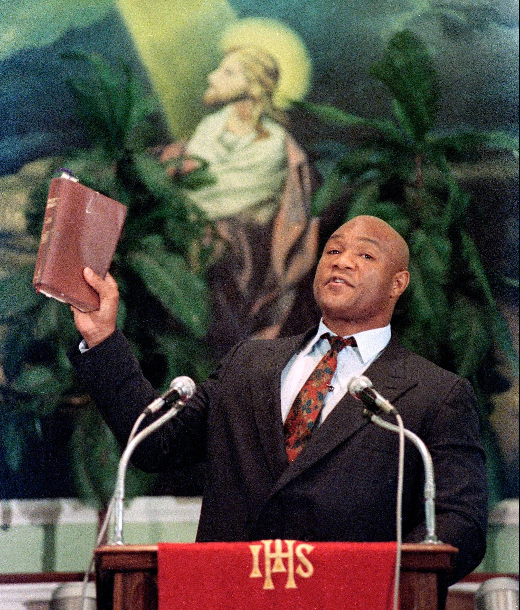 preach 桌布 壁紙 — 一位身穿西裝的傳道人在講壇上高舉聖經，背後有耶穌的畫像。