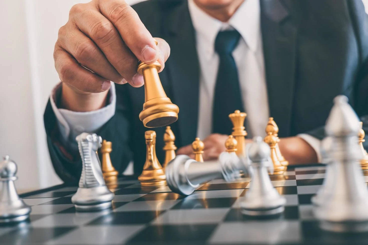 西洋棋 桌布 壁紙 — 一位身穿西裝的商人正在棋盤上移動一枚金色棋子，銀色棋子清晰對焦。