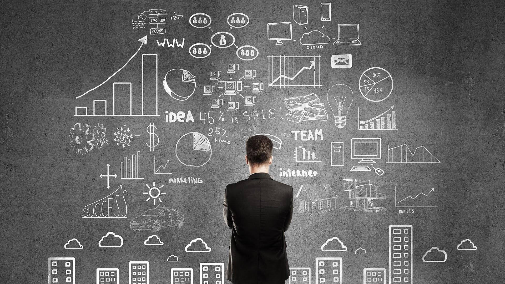Business 桌布 壁紙 — 一位身穿西裝的商人站在一面佈滿白色商業圖表和圖標的黑板牆前，這些圖表和圖標代表策略、創新和增長。