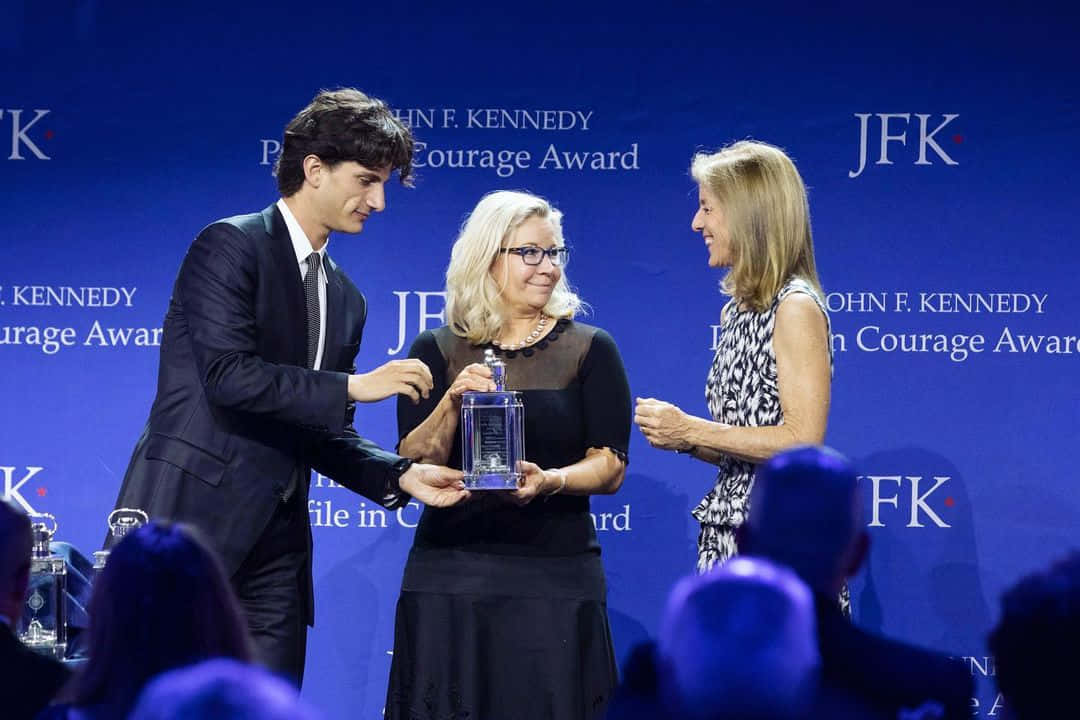 Celebrity 桌布 壁紙 — 一位身穿西裝的年輕男子在藍色舞台背景上，帶有JFK Courage Award文字，向一位年長女性頒發玻璃獎項。
