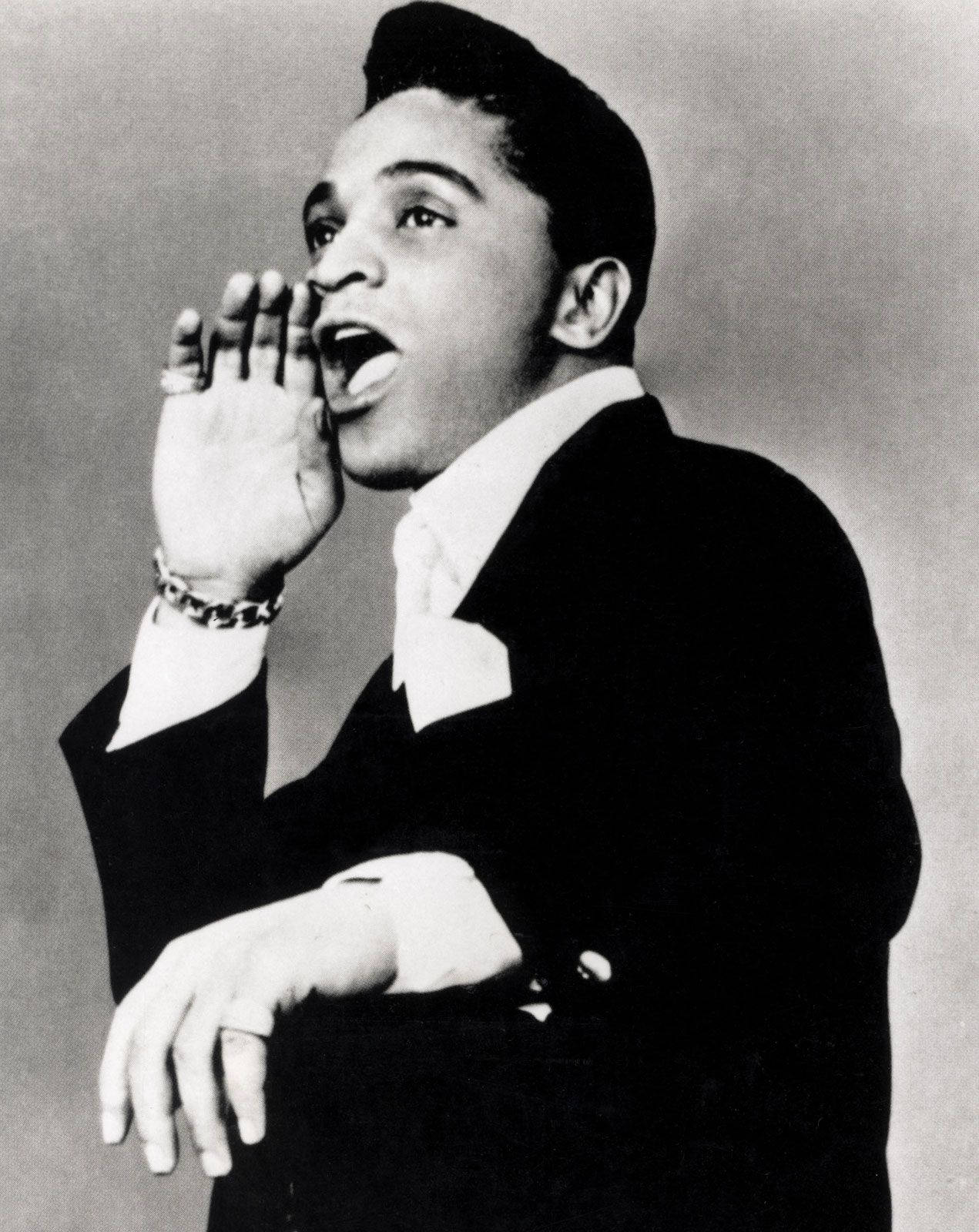 Singer 桌布 壁紙 — 一位身穿西裝的年輕男子對著合攏的手掌大喊，背景是簡約的攝影棚，形成一張戲劇性的黑白肖像。