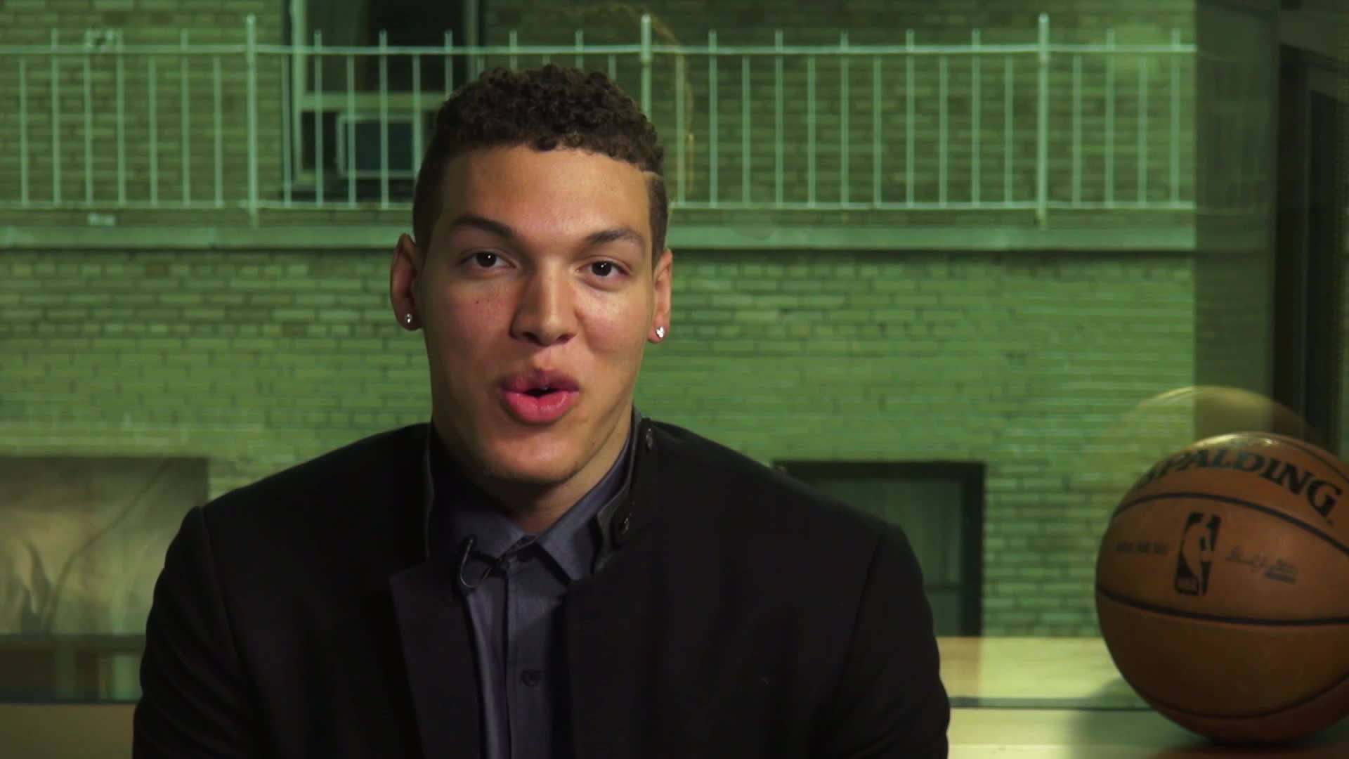 aaron gordon 桌布 壁紙 — 一位身穿西裝的年輕籃球運動員坐在綠色磚牆前，旁邊放著一個Spalding籃球。