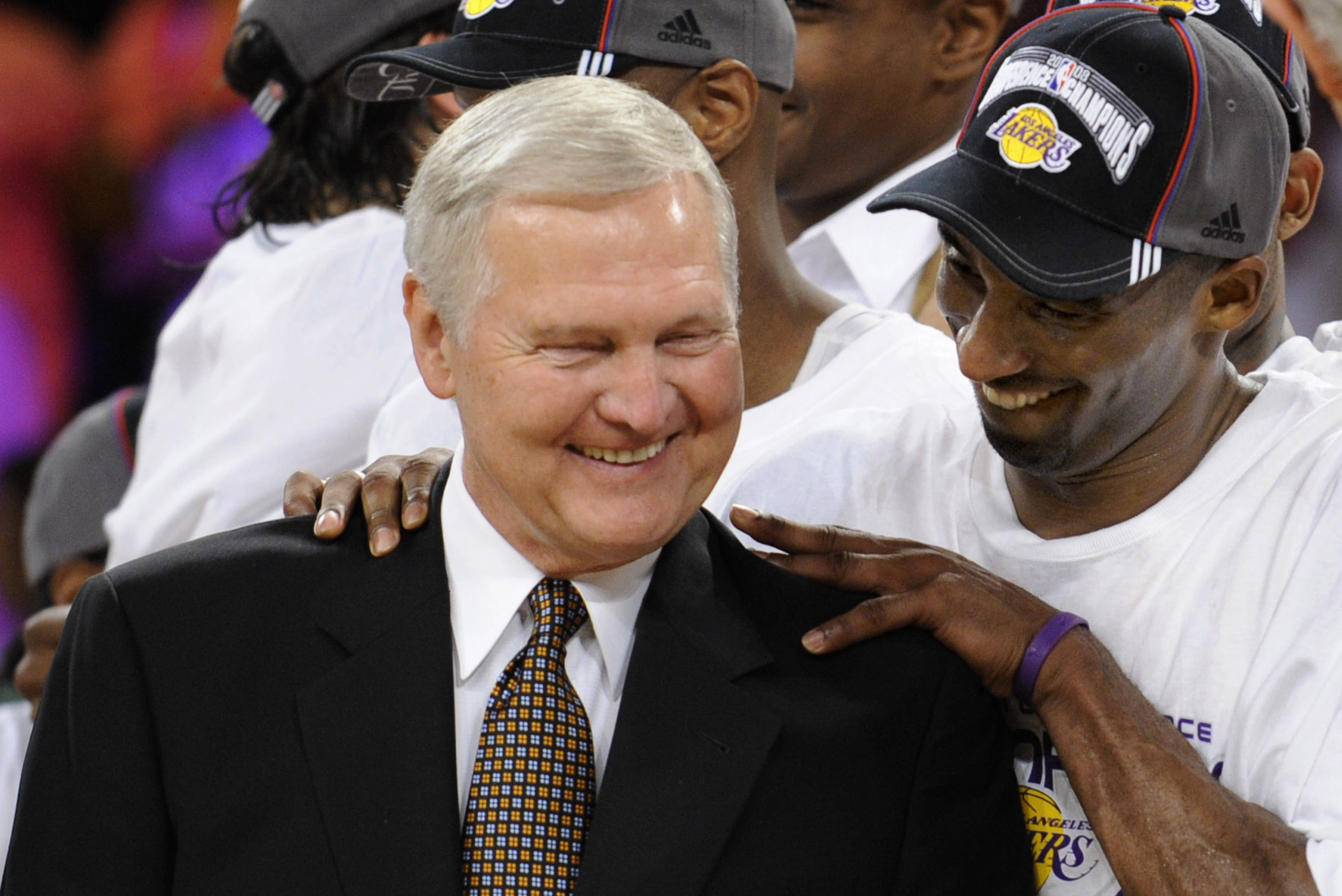 NBA 桌布 壁紙 — 一位身穿西裝的快樂籃球教練笑容滿面，一名戴著湖人隊帽子的球員深情地將手放在教練的肩膀上。