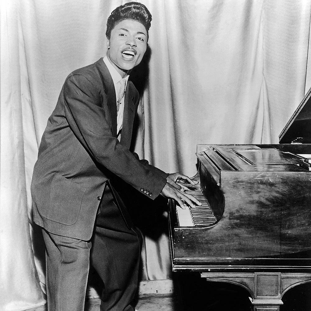 Singing 桌布 壁紙 — 一位身穿西裝的快樂黑人男子在表演中俯身於三角鋼琴上，背景是垂簾。
