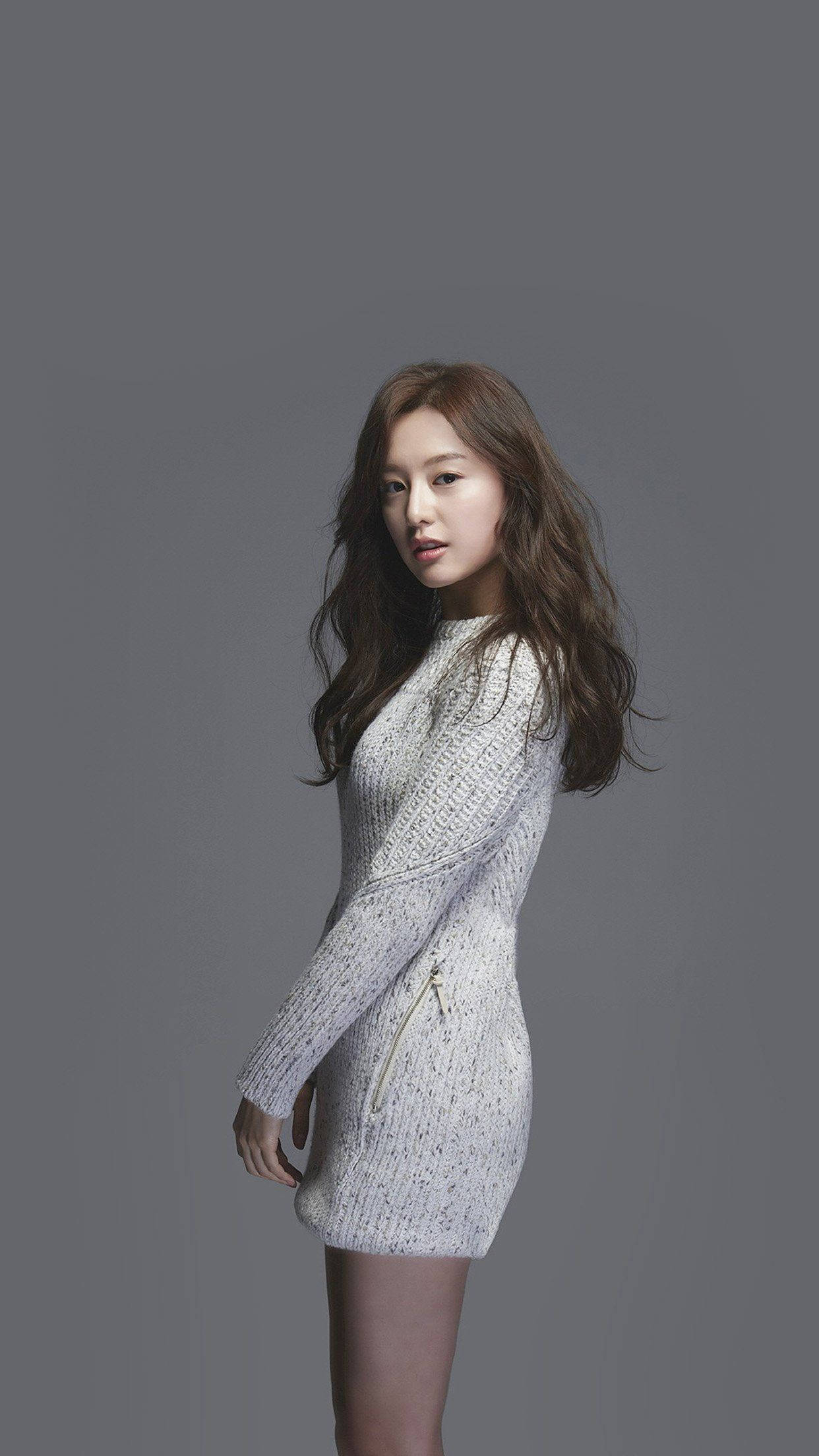 K-pop 桌布 壁紙 — 一位身穿質感白色針織連衣裙的女性在柔和的燈光下，在純灰色工作室背景前擺姿勢。
