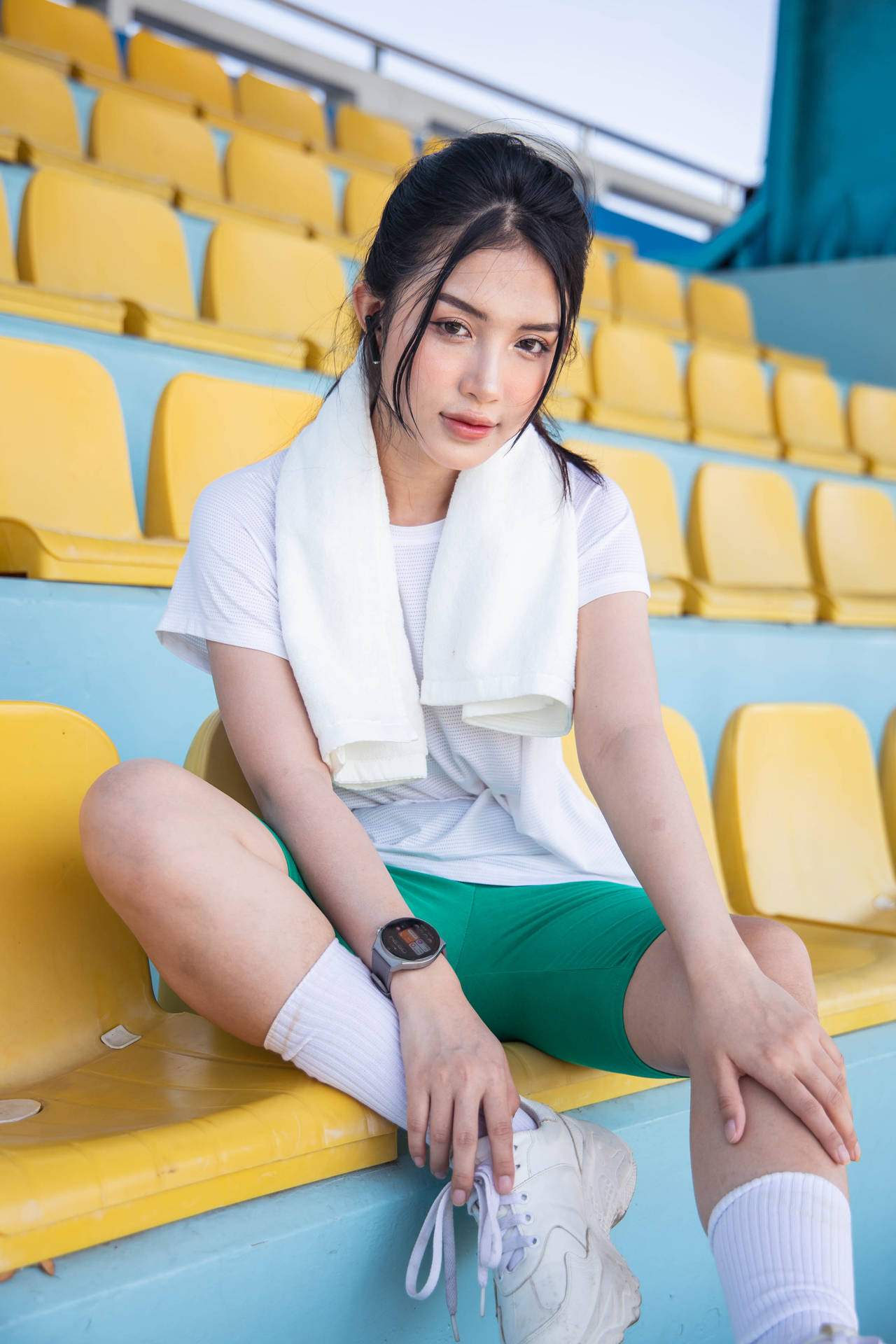 身穿運動服的年輕女性坐在體育場座位上，脖子上圍著毛巾。 — 智慧手錶 GIF 壁紙