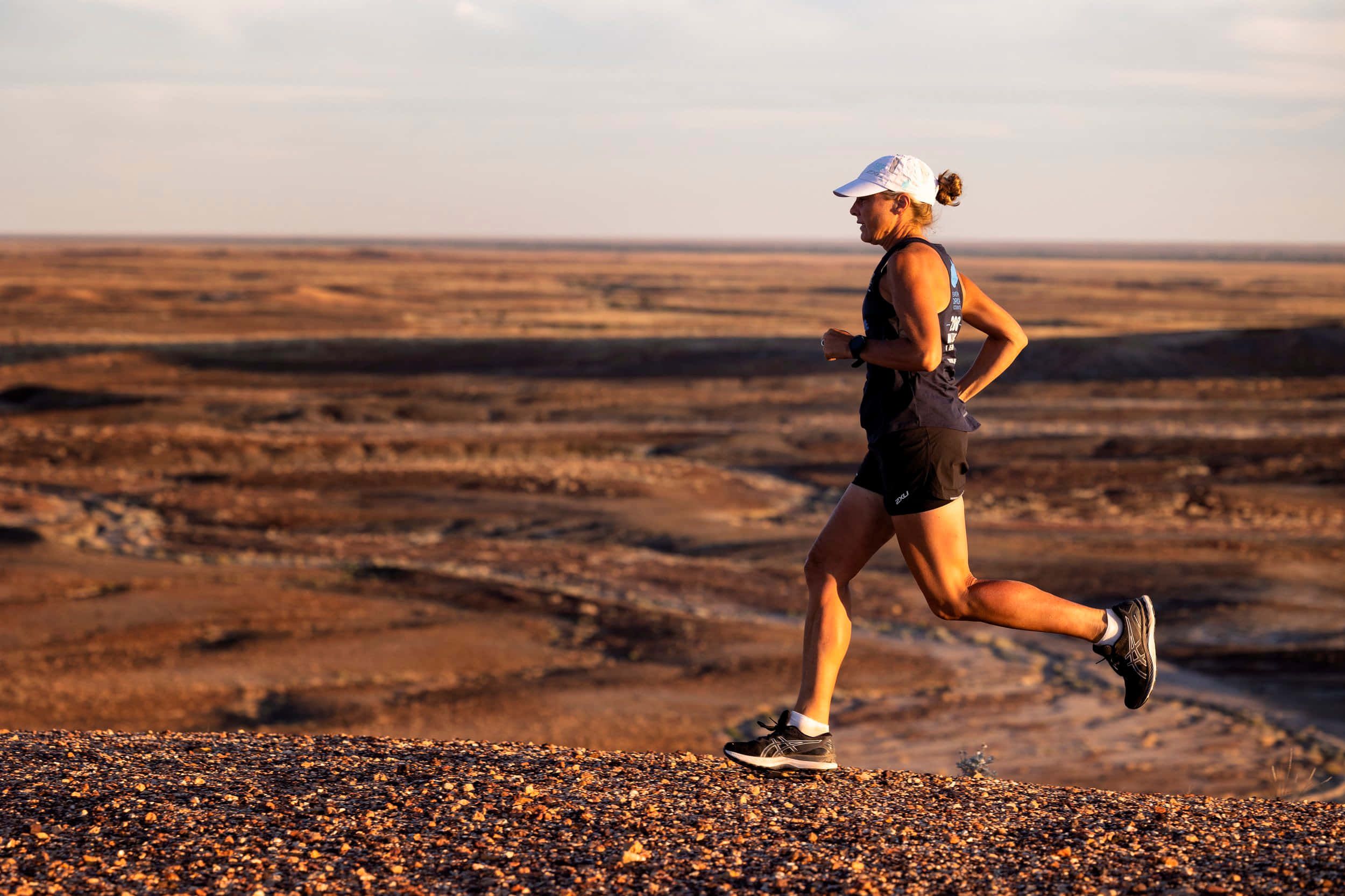 Running 桌布 壁紙 — 一位身穿運動裝備的女跑者在金色日落光芒下，於廣闊乾旱的景觀中衝刺。