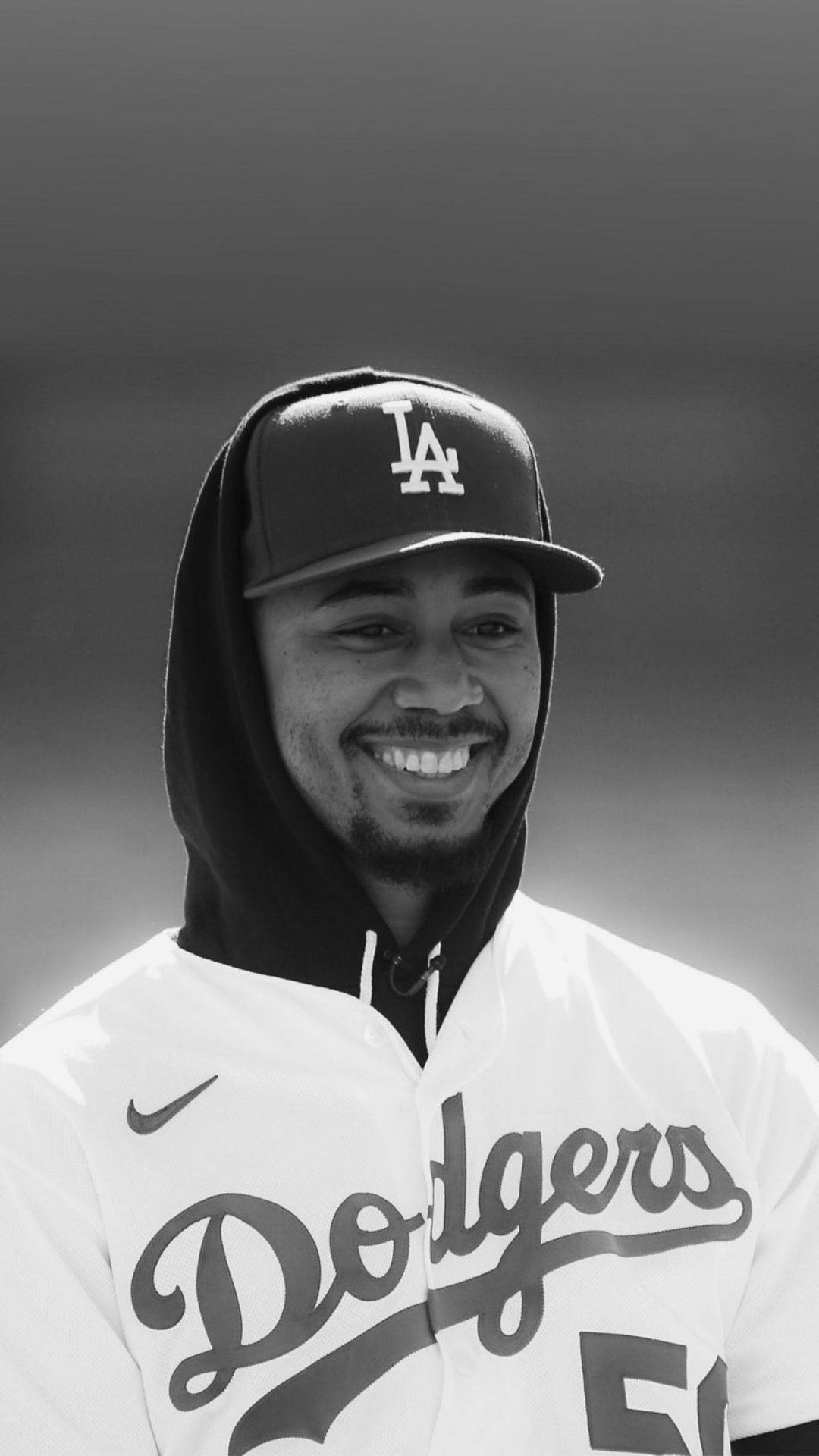 Mookie Betts 桌布 壁紙 — 一位身穿道奇隊制服和帽子的微笑棒球運動員，在模糊背景的黑白肖像中閃耀。