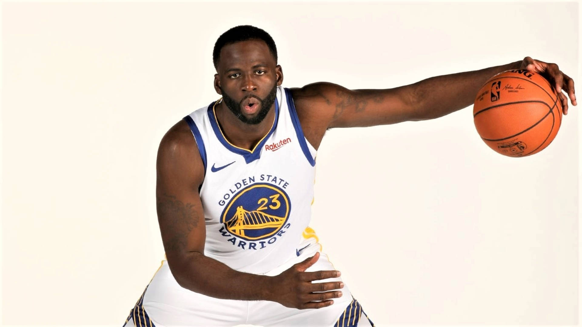 Draymond Green 桌布 壁紙 — 一位身穿金州勇士隊球衣的籃球運動員在純色背景前以動態姿勢持球。