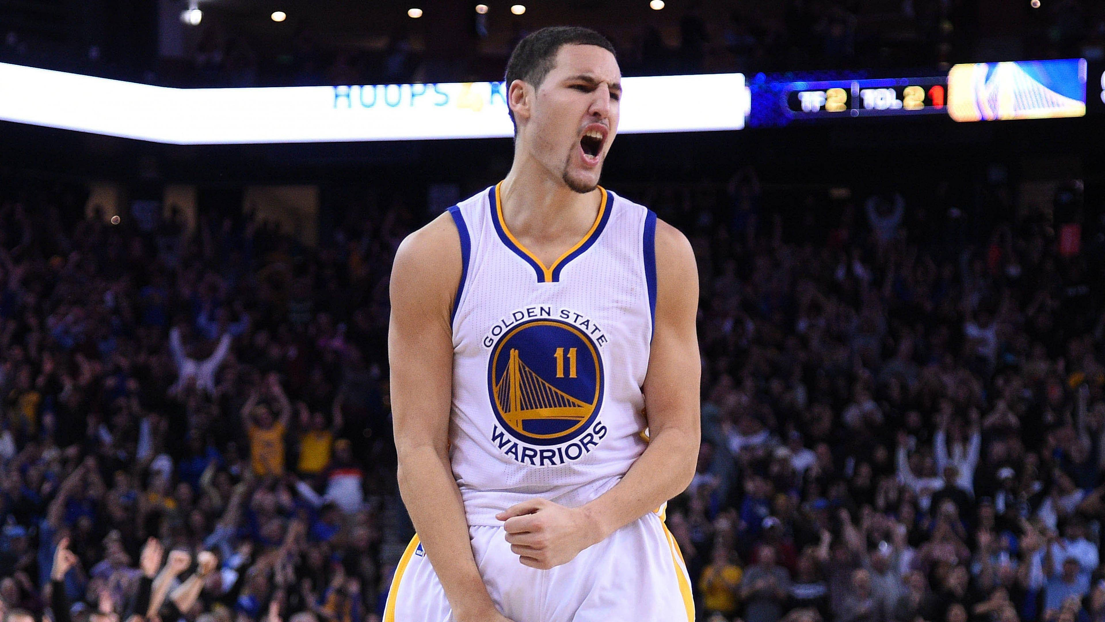 Thompson 桌布 壁紙 — 一位身穿金州勇士隊球衣的籃球運動員在明亮的場館燈光下，在比賽中激烈咆哮。