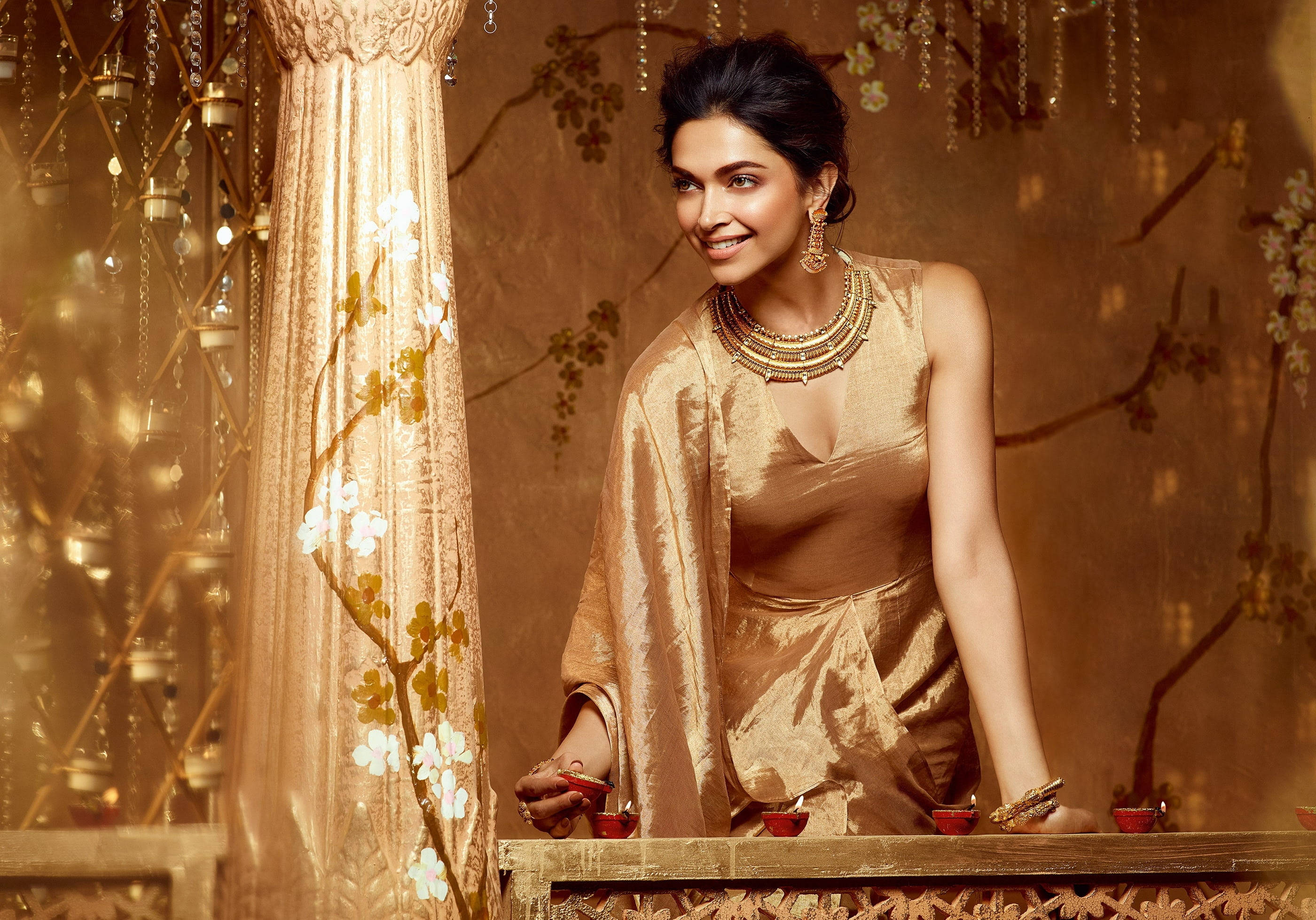 Deepika 桌布 壁紙 — 一位身穿金色傳統服飾的女性在裝飾華麗的桌子旁微笑，桌上擺有燃燒的蠟燭和花卉布簾。