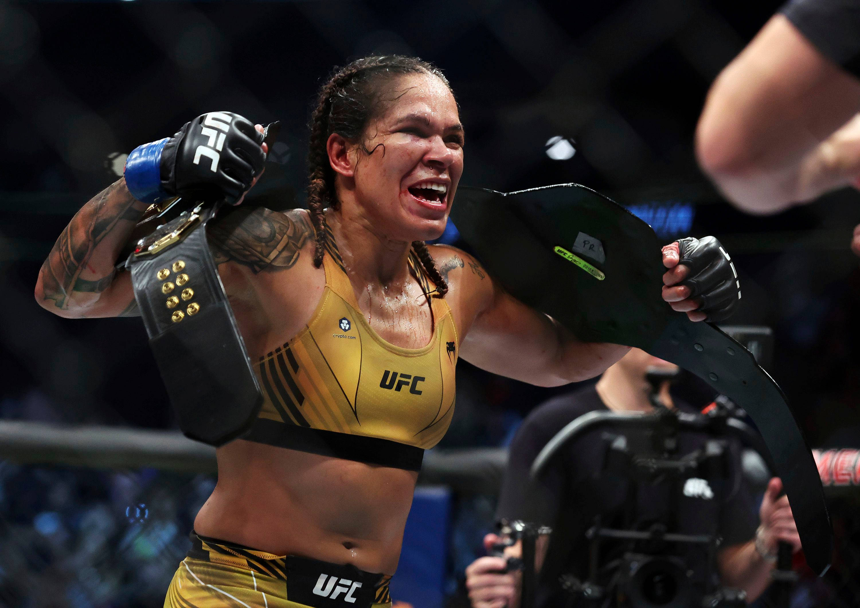 Champion 桌布 壁紙 — 一位身穿金色制服、勝利的女性UFC拳手在八角籠內高舉冠軍腰帶慶祝勝利。