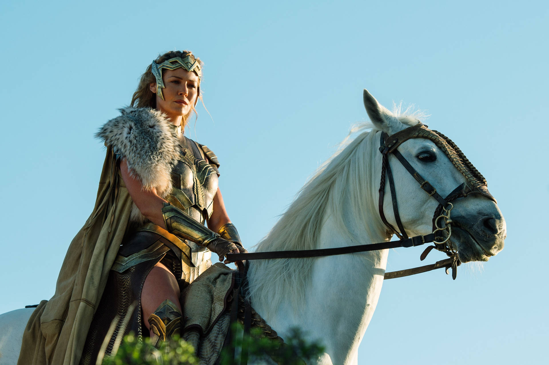 Wonder Woman 桌布 壁紙 — 一位身穿金色盔甲的女戰士騎著一匹雄偉的白馬，背景是晴朗的藍天。