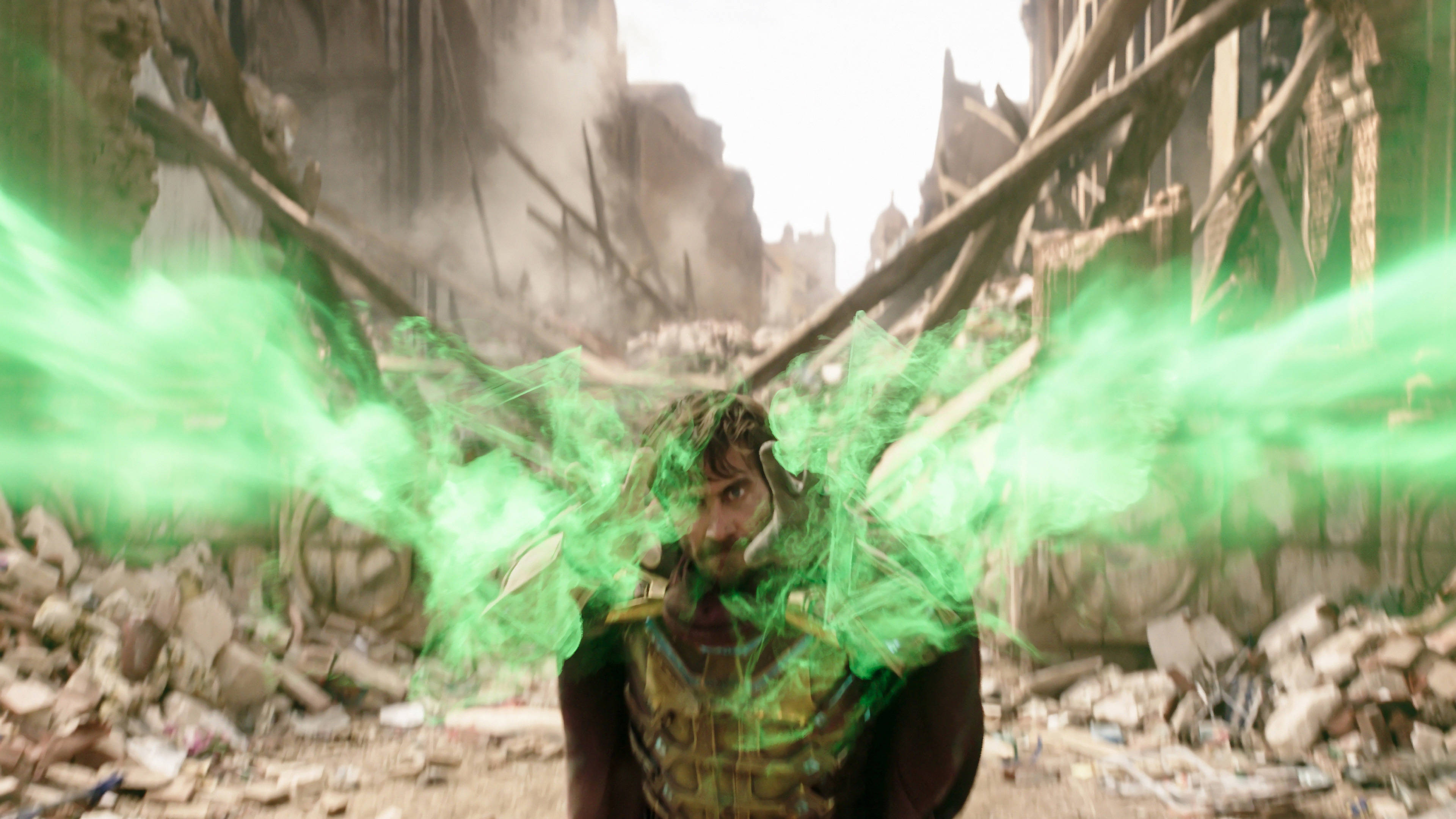 Mysterio 桌布 壁紙 — 一位身穿金色盔甲的超級英雄在破碎的石頭和扭曲的金屬構成的廢墟城市景觀中釋放出發光的綠色能量爆炸。