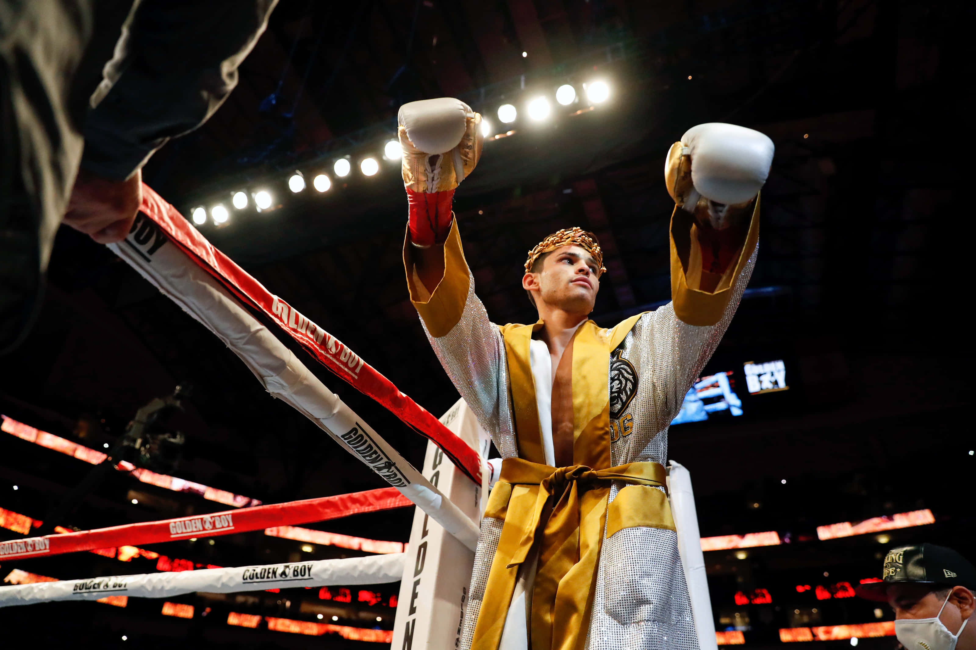 Boxing Gloves 桌布 壁紙 — 一位身穿金銀色長袍的勝利拳擊手在燈光明亮的擂台上高舉戴著手套的拳頭慶祝勝利。
