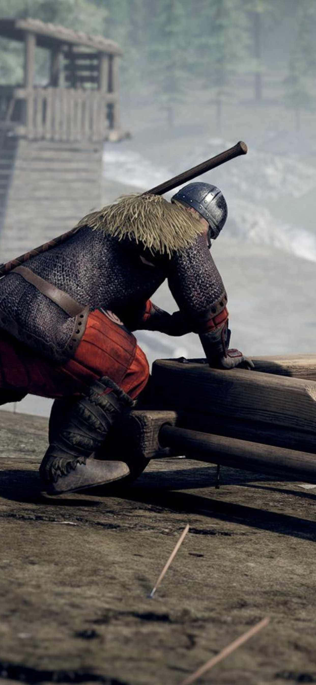 iPhone Xs Max Mordhau 桌布 壁紙 — 一位身穿鎖子甲和頭盔的中世紀騎士，在霧氣瀰漫的林間空地中跪在一台木製攻城器械旁。