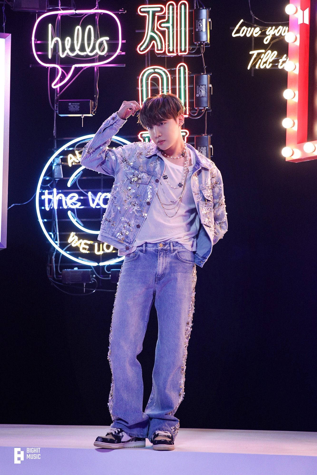 jhope 桌布 壁紙 — 一位身穿閃亮牛仔外套和牛仔褲的年輕男子，在充滿活力的霓虹燈背景和發光標誌前自信地擺姿勢。