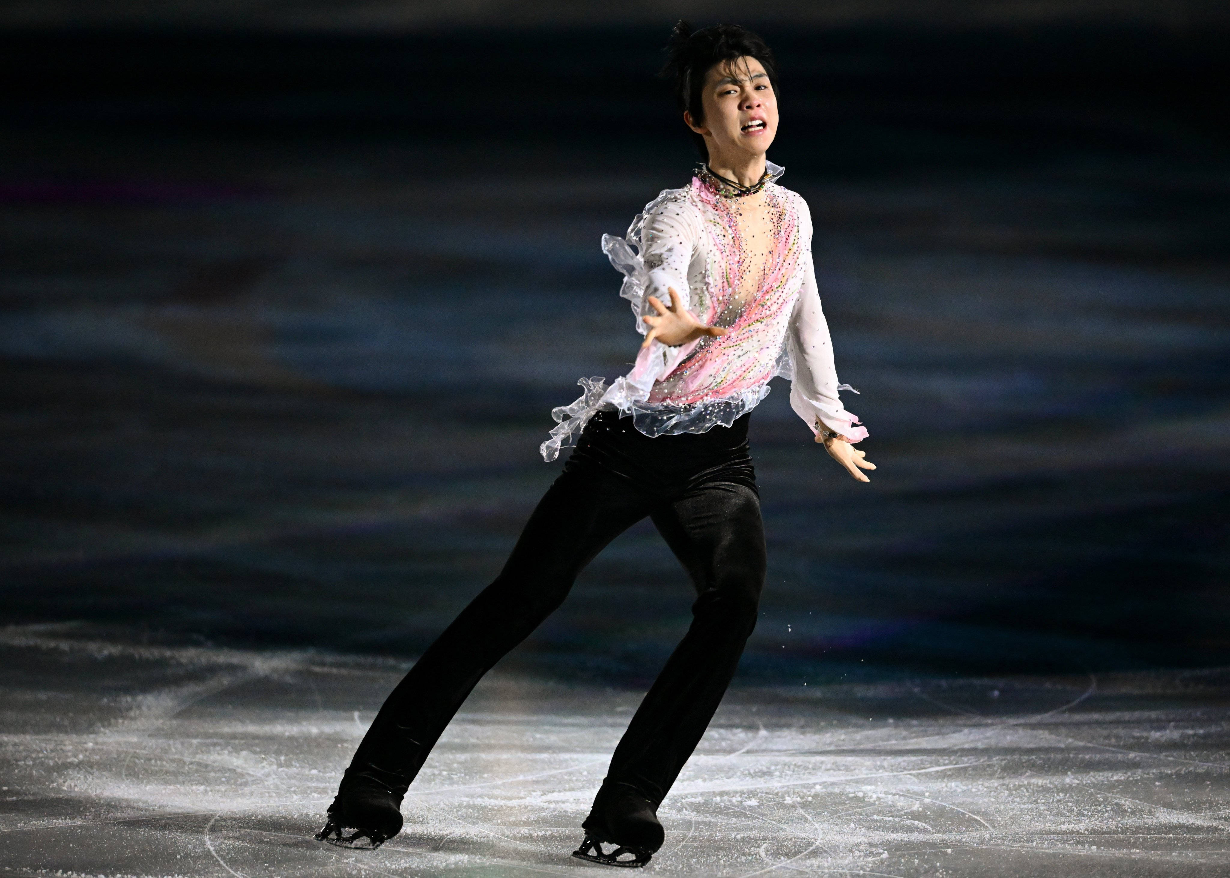 Olympics 桌布 壁紙 — 一位身穿閃亮白色和粉紅色服裝的花式滑冰選手，在戲劇性的舞台燈光下，動態地滑過冰場。