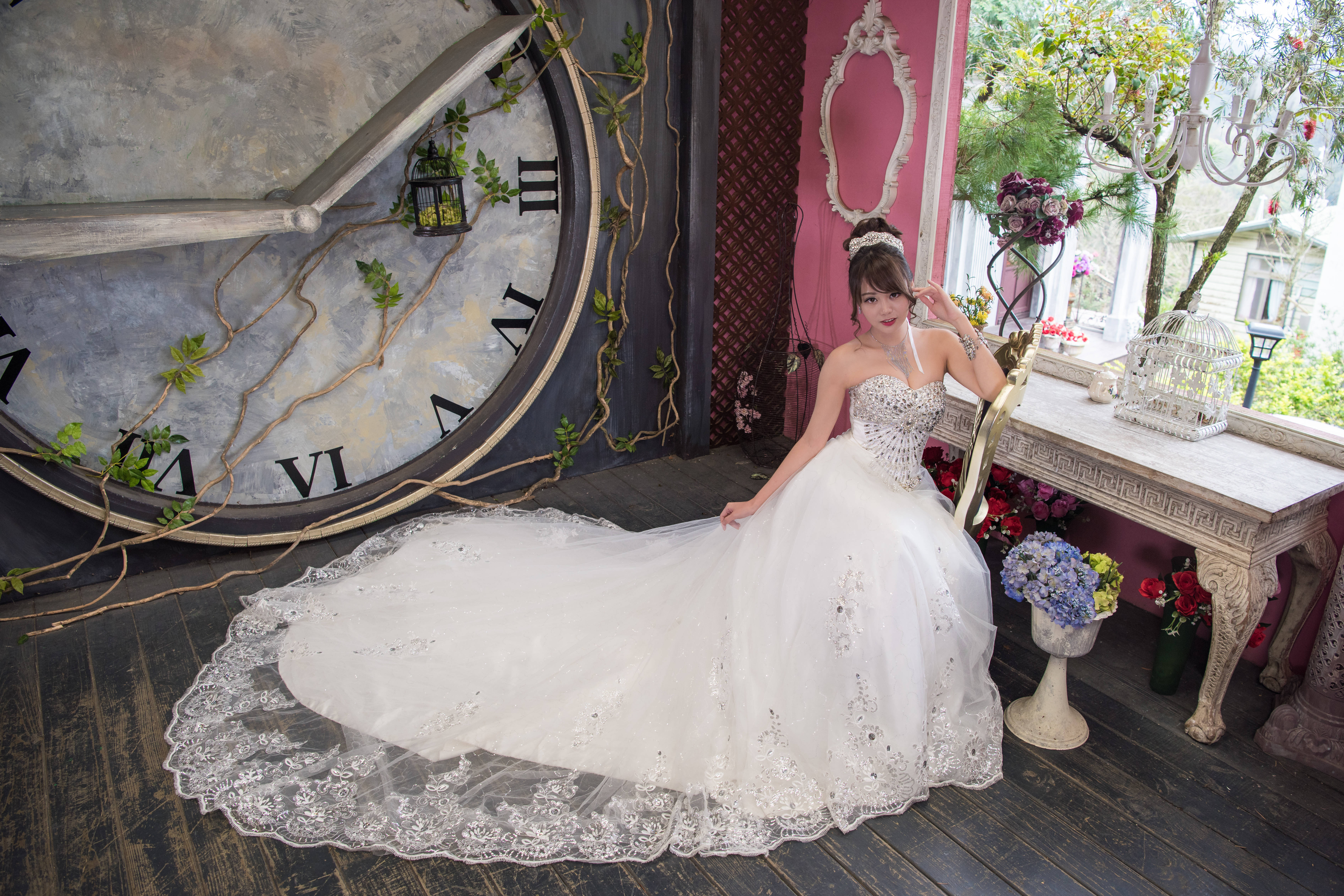 Bride 桌布 壁紙 — 一位身穿閃亮白色婚紗的女性優雅地坐在一個纏繞著綠色藤蔓的巨大復古時鐘旁。