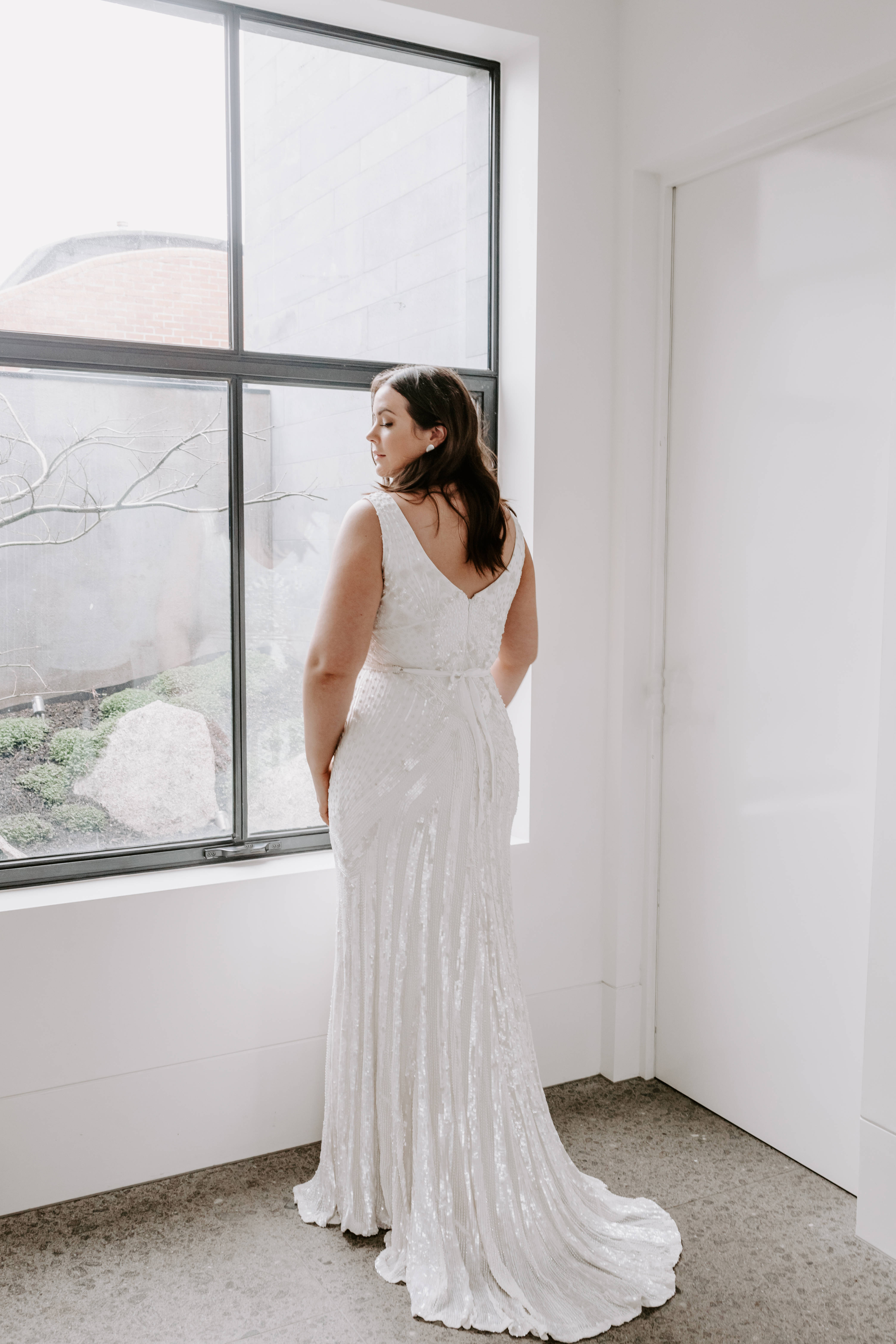 Wedding Aesthetic 桌布 壁紙 — 一位身穿閃亮白色婚紗的女性站在大窗戶旁，在極簡白色房間內向外凝望。