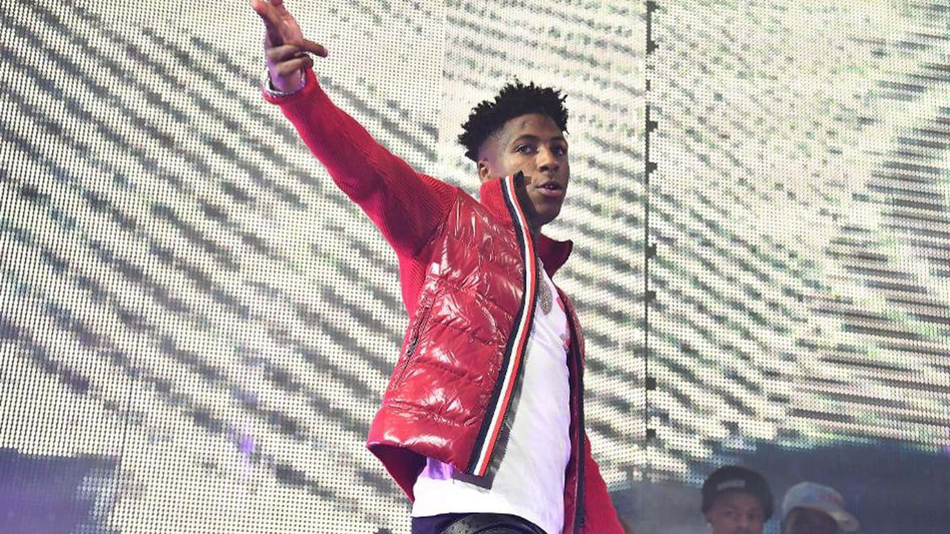 NBA YoungBoy 桌布 壁紙 — 一位身穿閃亮紅色外套的表演者在舞台上舉起手，身後是像素化的LED牆。
