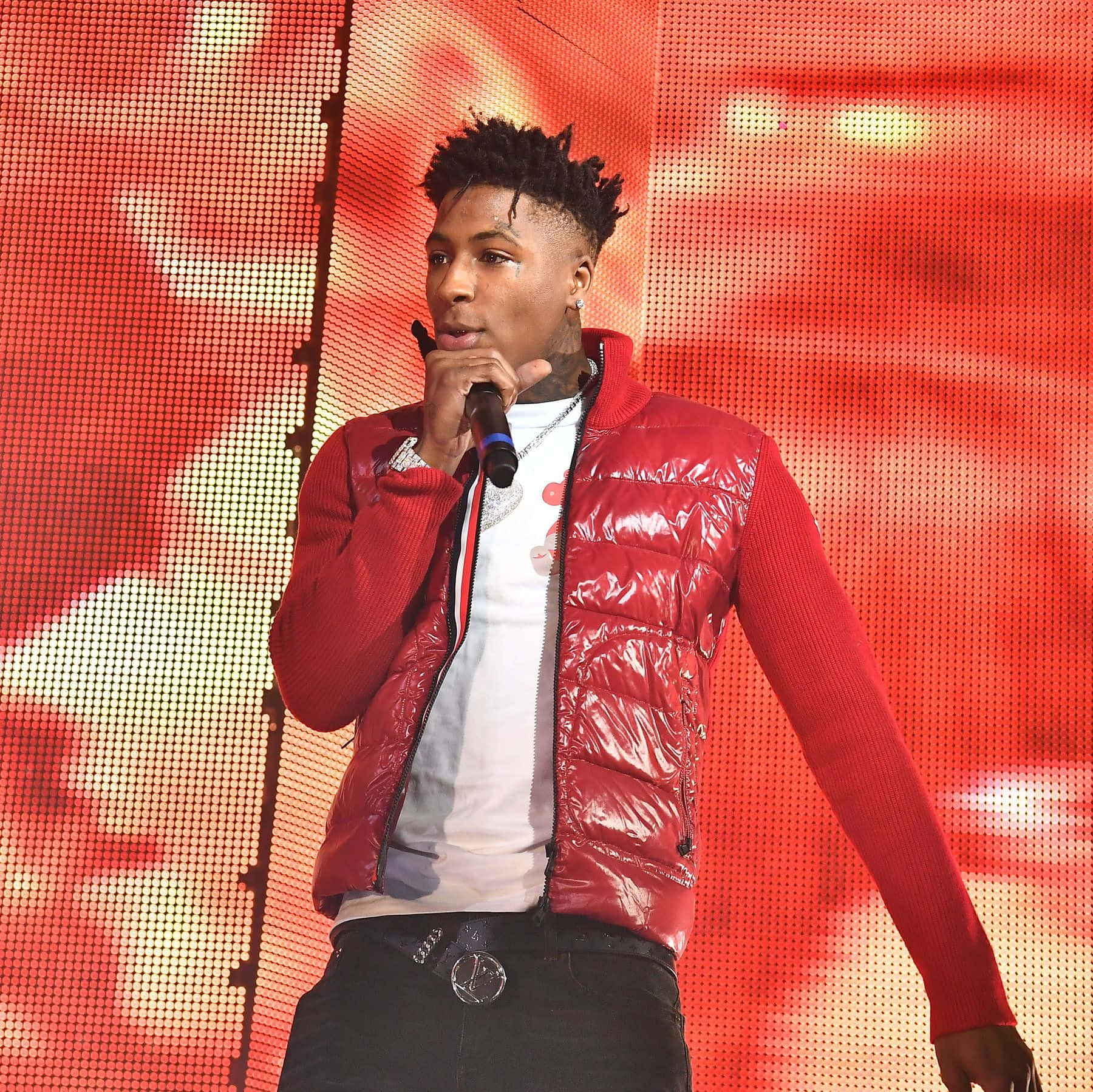 Youngboy 桌布 壁紙 — 一位身穿閃亮紅色背心的男表演者，在充滿活力的紅色像素化舞台背景前對著麥克風唱歌。